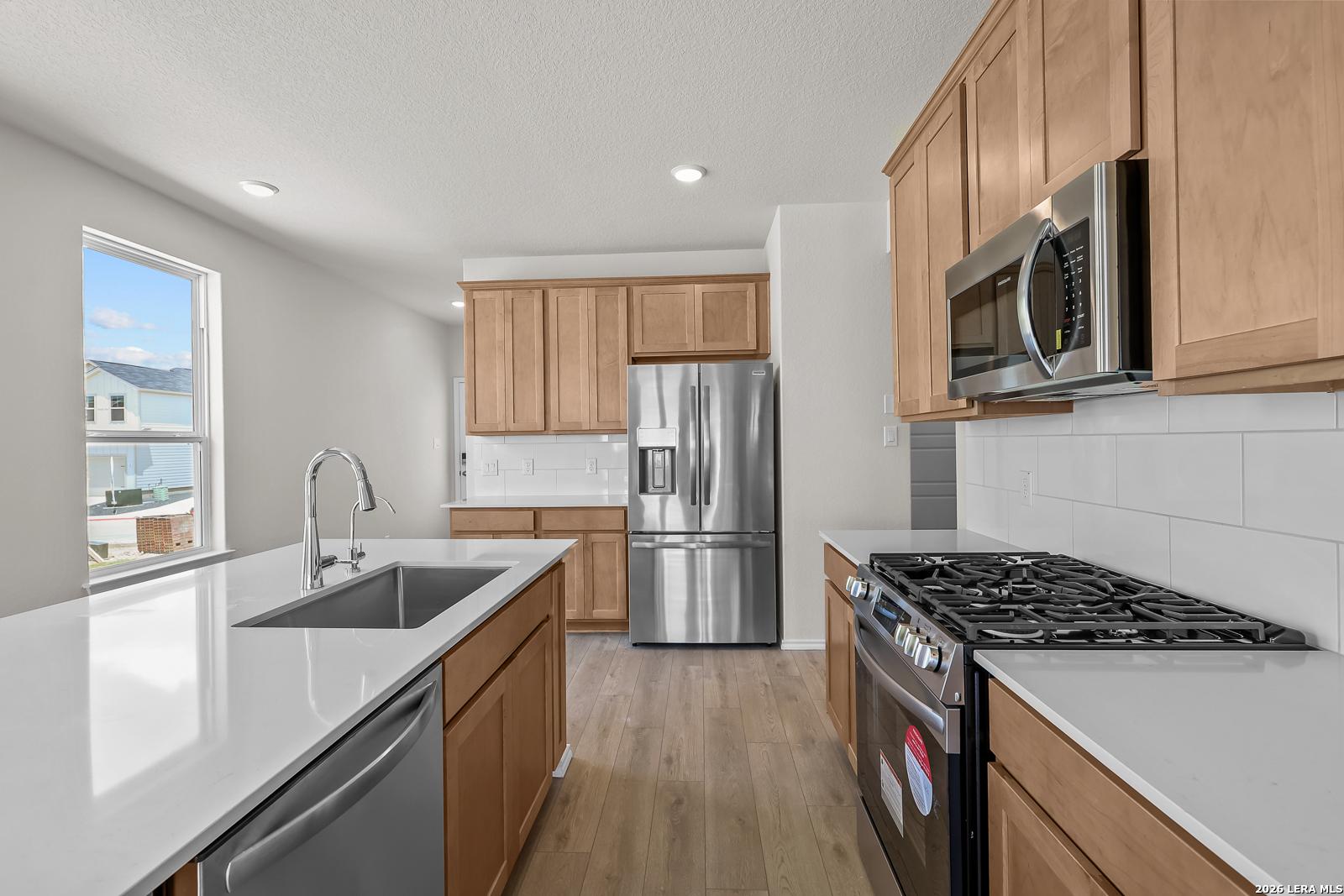 Modern kitchen with white quartz countertops, stainless steel appliances, and wood cabinets in The Gillian B floor plan.