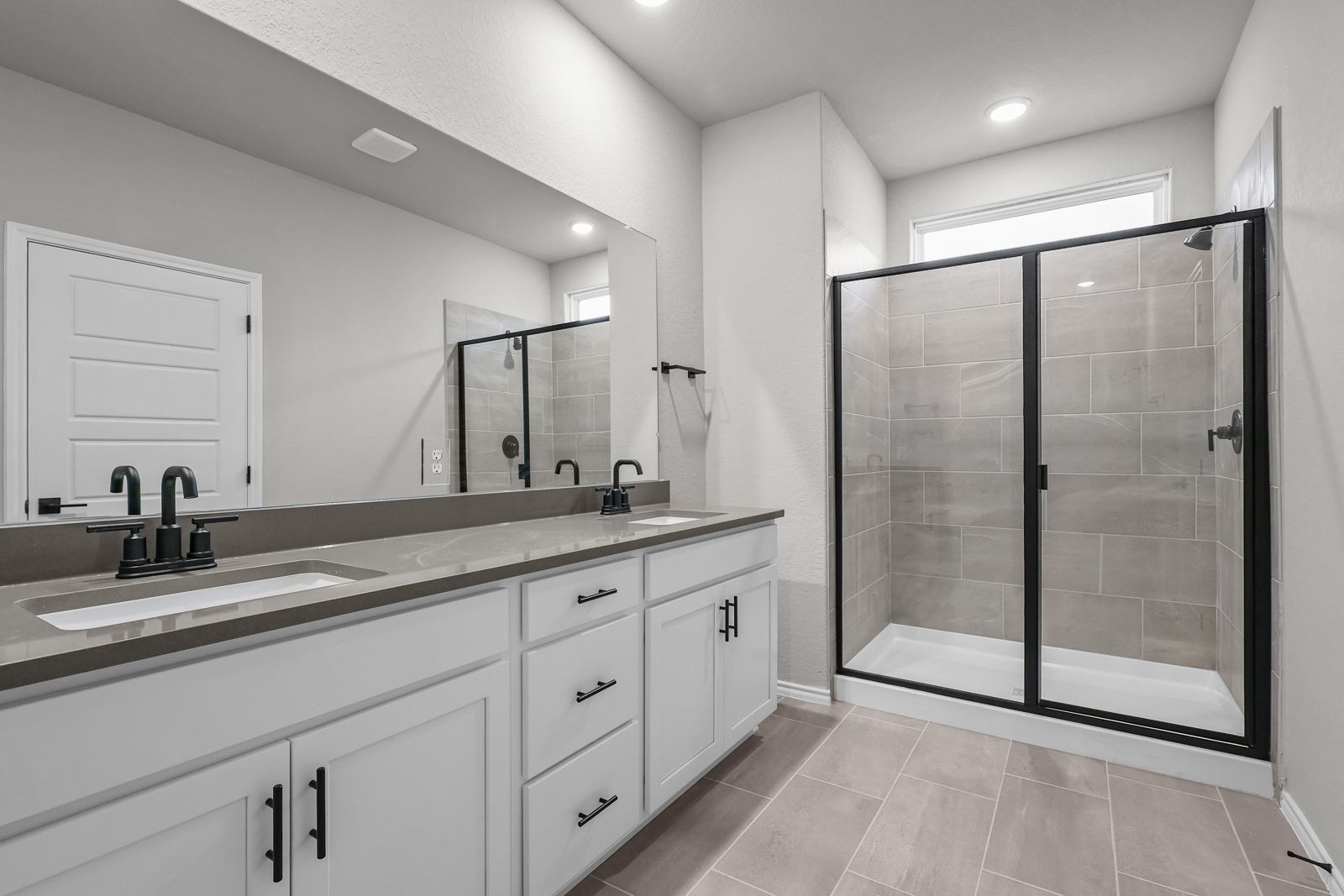 Modern master bathroom in The Glenwood E featuring a dual-sink vanity and a walk-in glass shower with black fixtures.