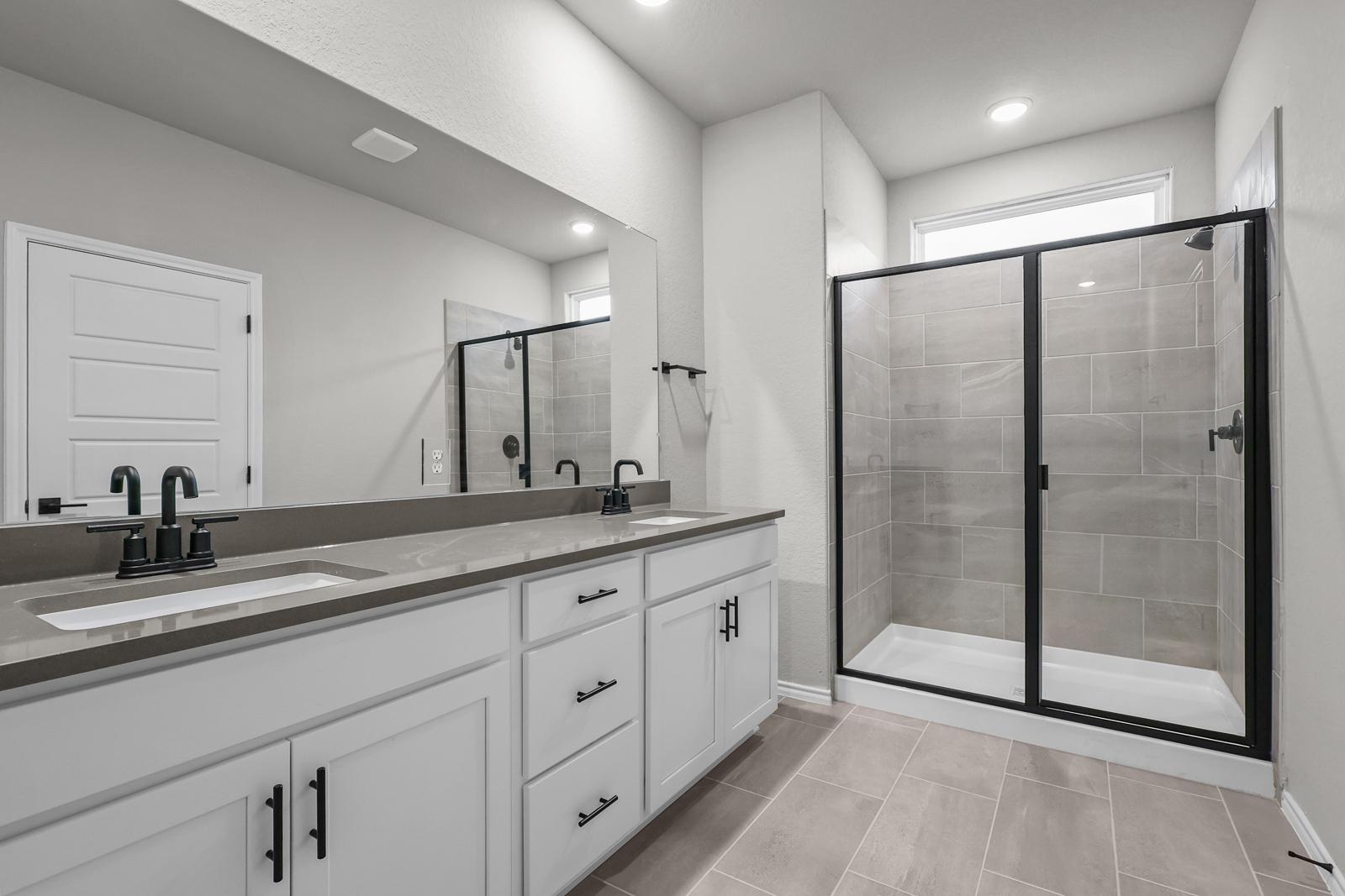 Modern master bathroom in The Glenwood E featuring a dual-sink vanity and a walk-in glass shower with black fixtures.