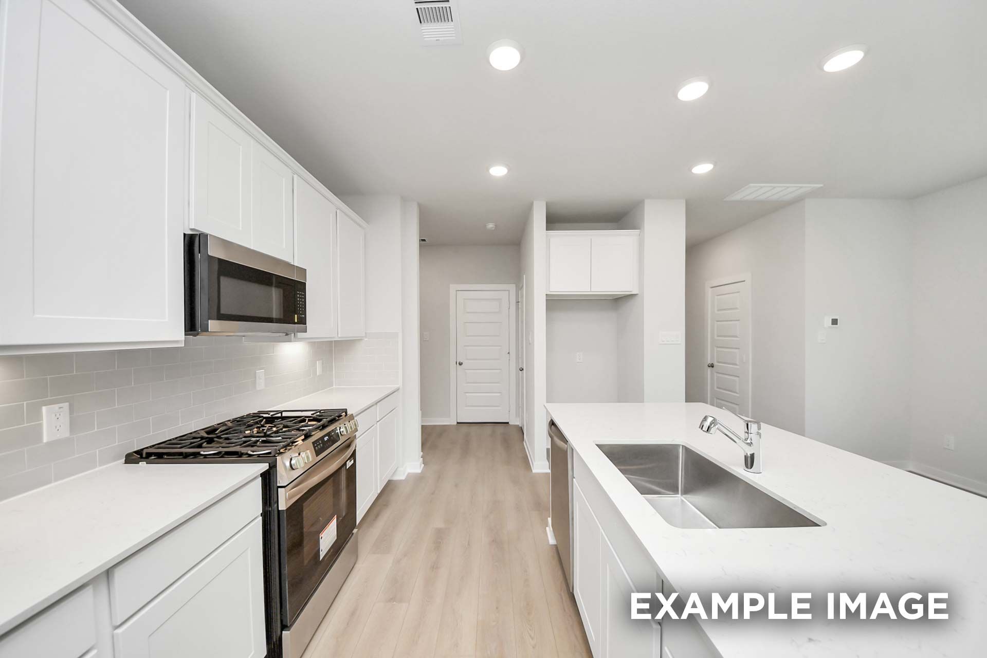 Bright kitchen in The Blanco by Davidson Homes with white cabinetry, island sink, gas range, and stainless appliances