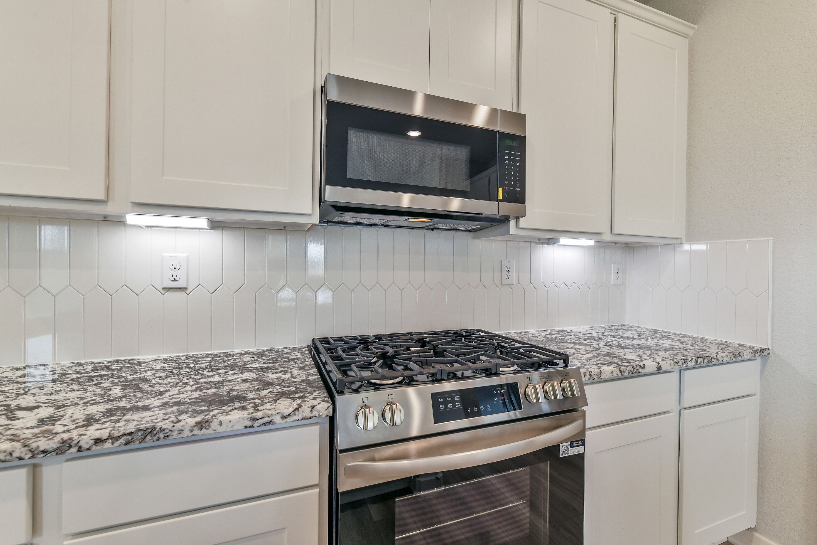 Modern kitchen with white shaker cabinets, speckled granite counters, stainless gas range and microwave in Davidson Homes The Colorado G, Magnolia TX
