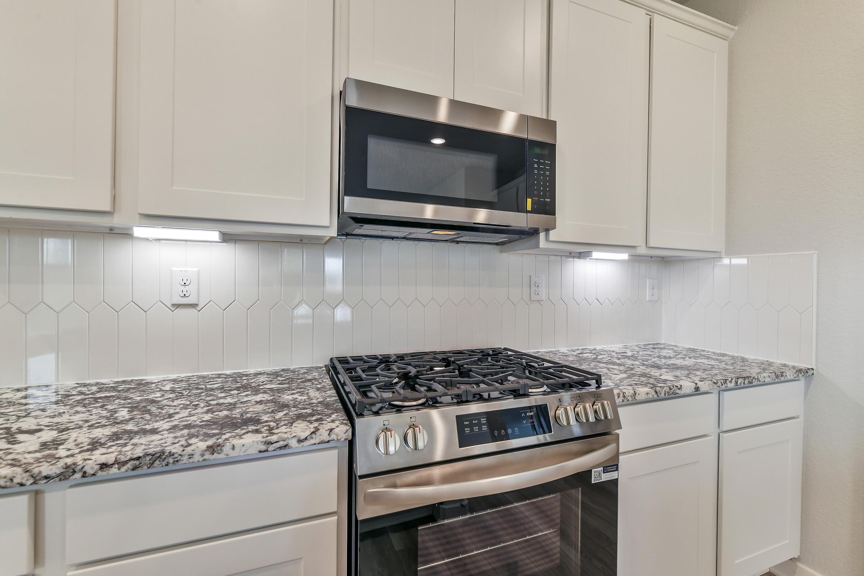 Modern kitchen with white shaker cabinets, speckled granite counters, stainless gas range and microwave in Davidson Homes The Colorado G, Magnolia TX