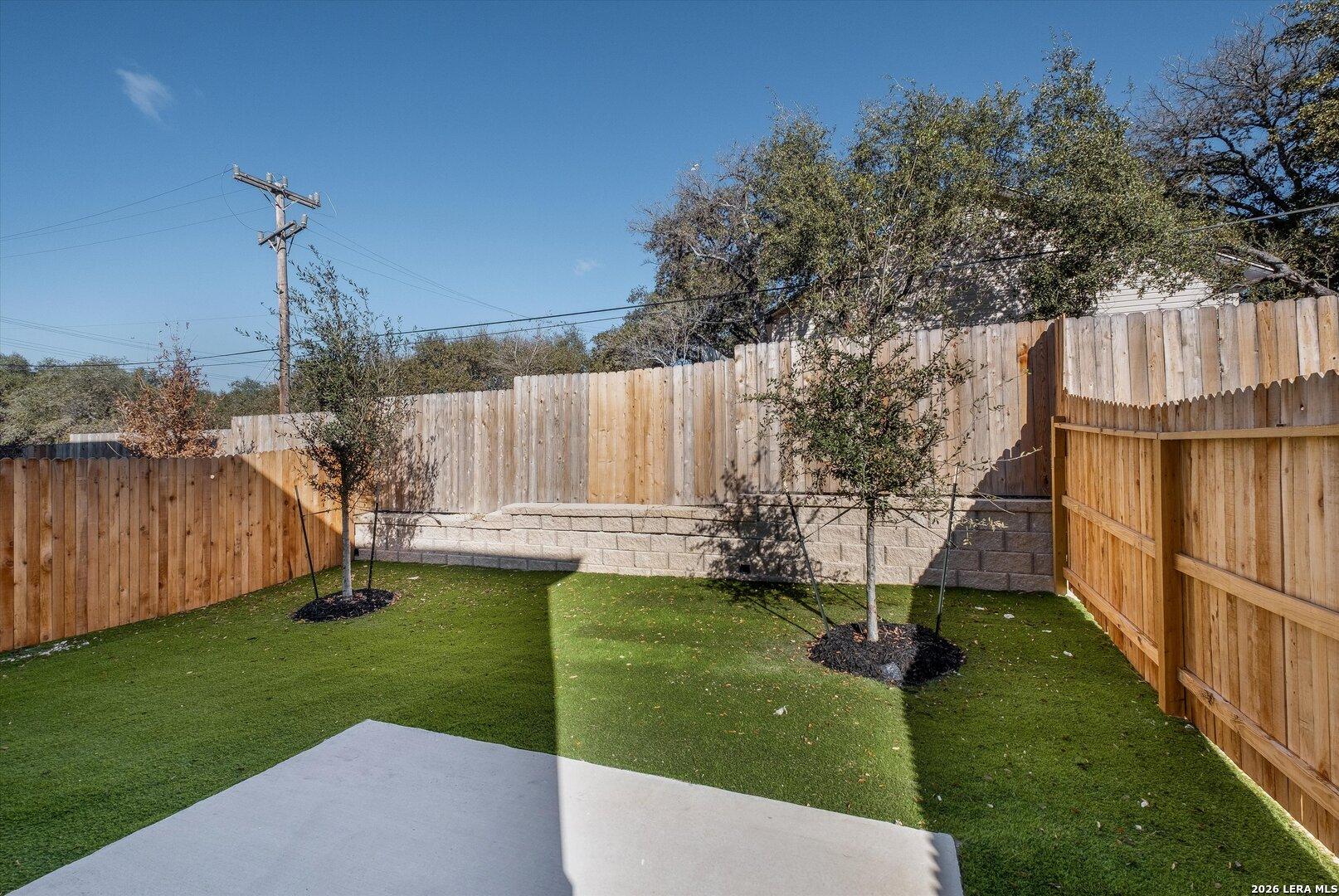 Private fenced backyard with green turf, young oaks, wooden privacy fence in Davidson Homes The Charlotte A, San Antonio, Texas
