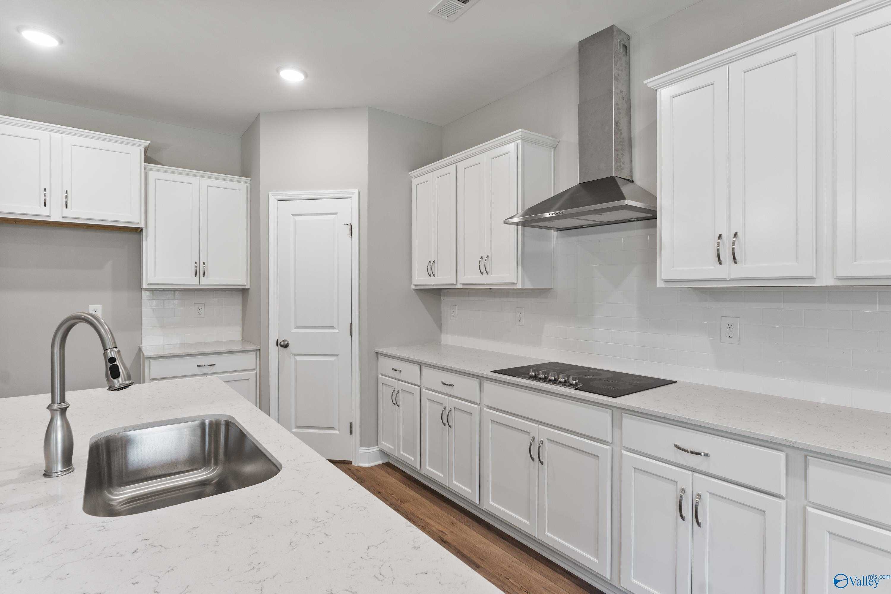 Modern white shaker kitchen with quartz island, stainless sink, and range hood in Davidson Homes The Rockford, Harvest, AL