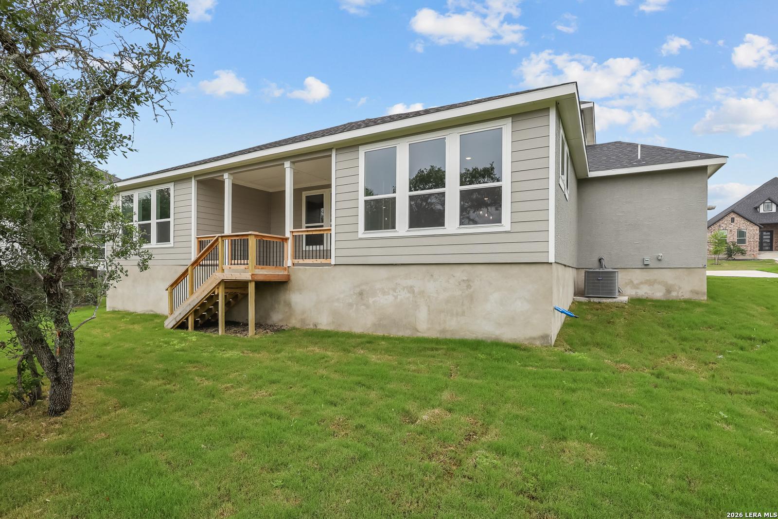 Two-story Belmont H home side view with wooden deck stairs, large windows, and lush green yard in Potranco Oaks, Castroville, Texas