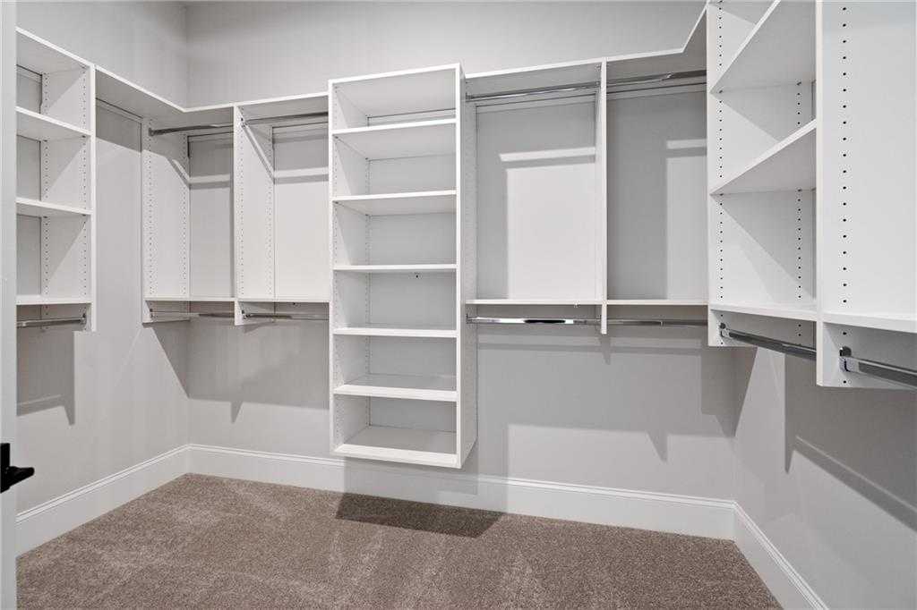 Spacious walk-in closet with white built-in shelves and hanging rods in Davidson Homes The Seaside B, Woodstock, Georgia