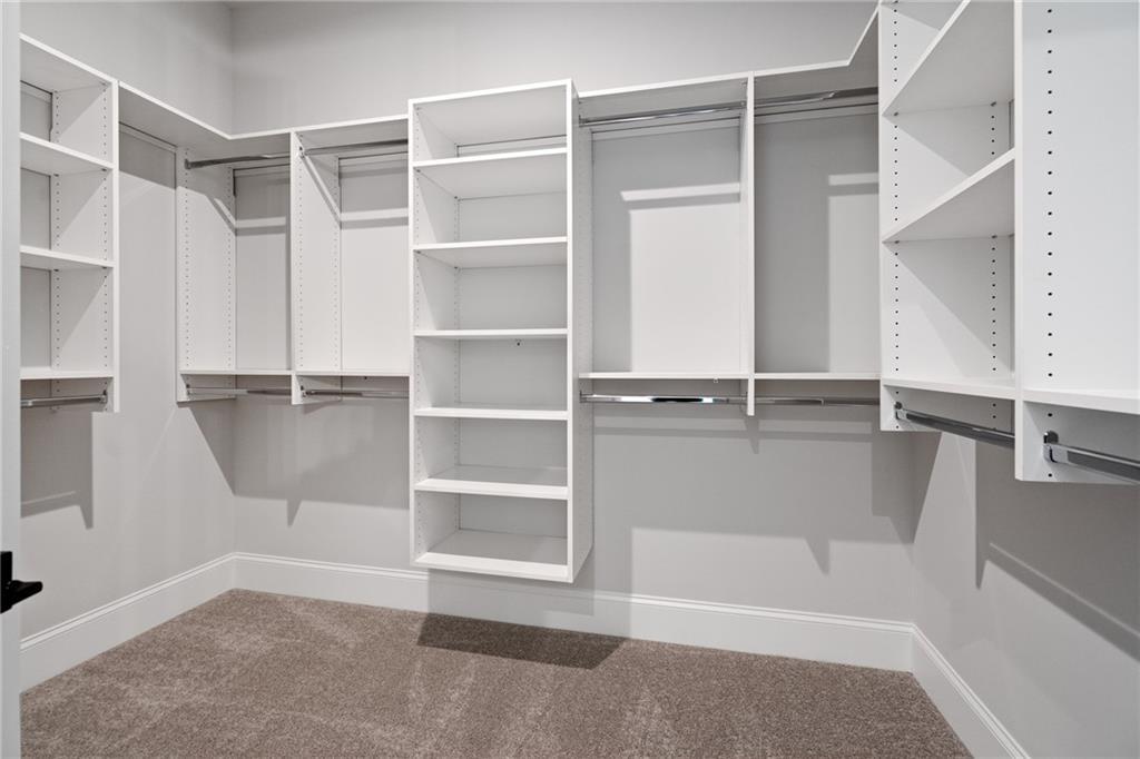 Spacious walk-in closet with white built-in shelves and hanging rods in Davidson Homes The Seaside B, Woodstock, Georgia