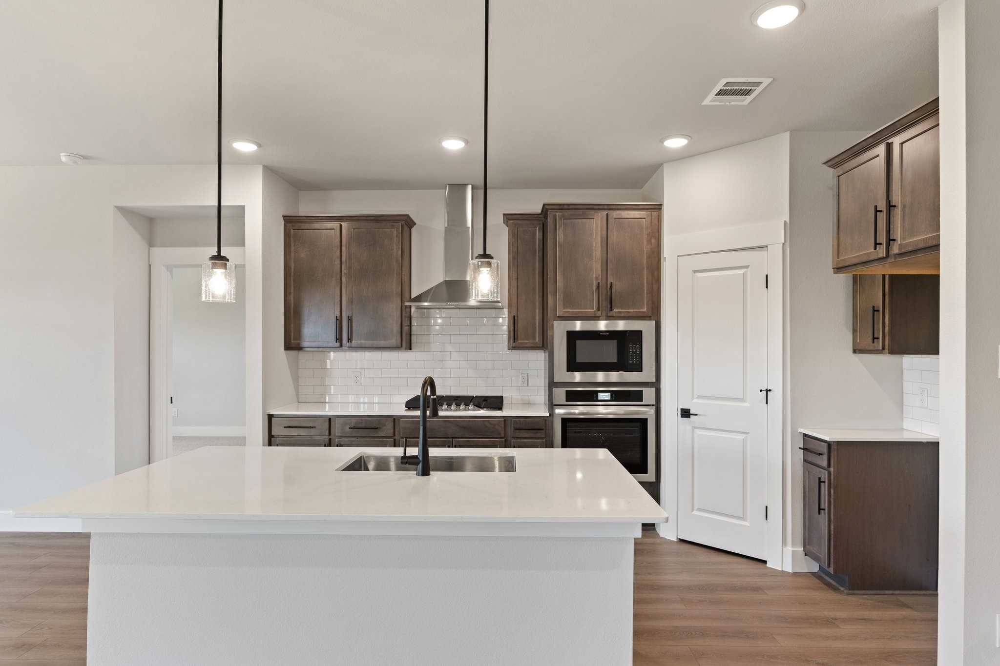 Modern kitchen with white quartz island, brown shaker cabinets, stainless appliances, subway tile backsplash in The Everett C, Josephine, Texas