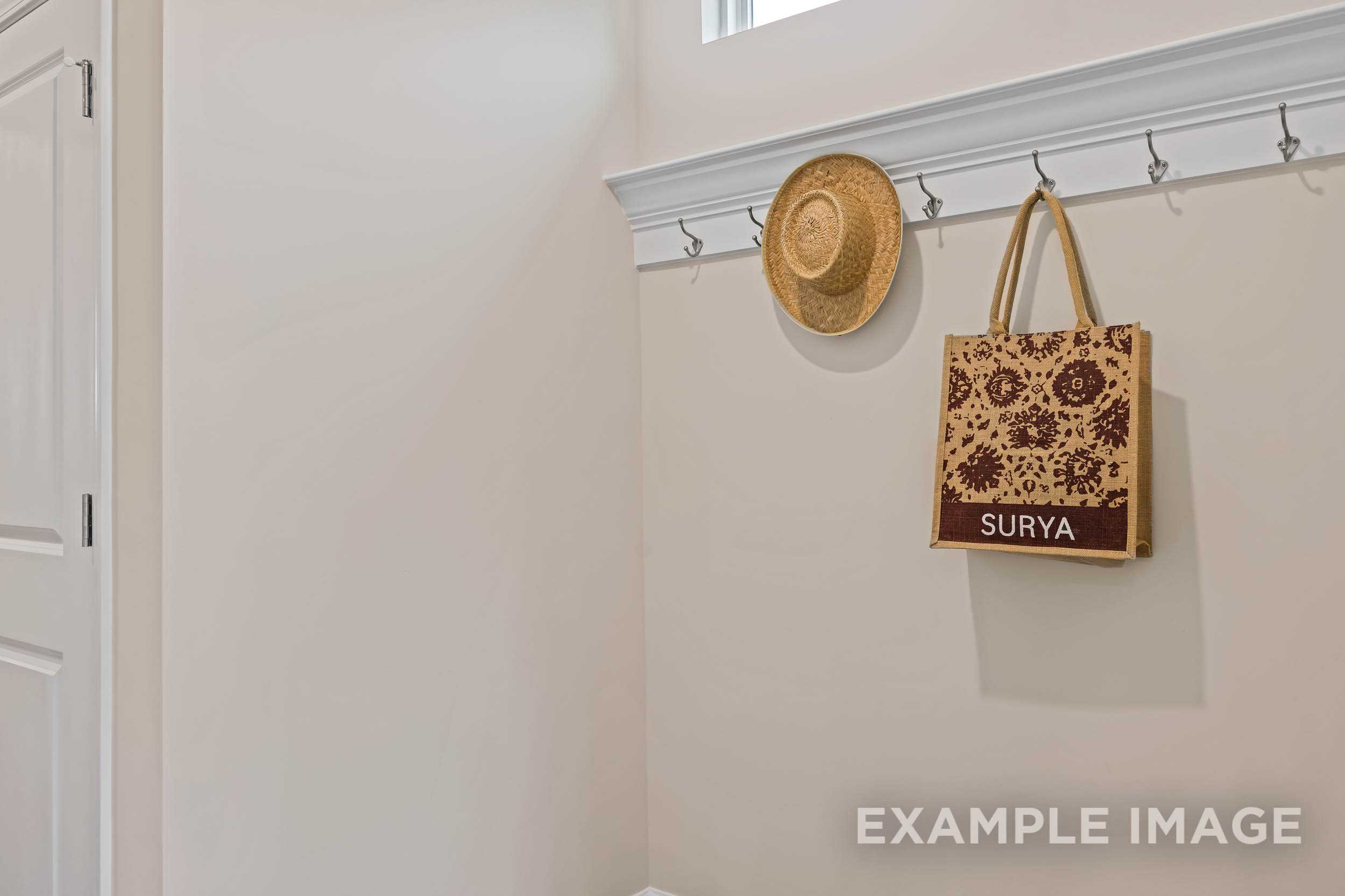 Cozy entryway in The Preston A home design with wall hooks holding straw hat and Surya tote bag on beige wall