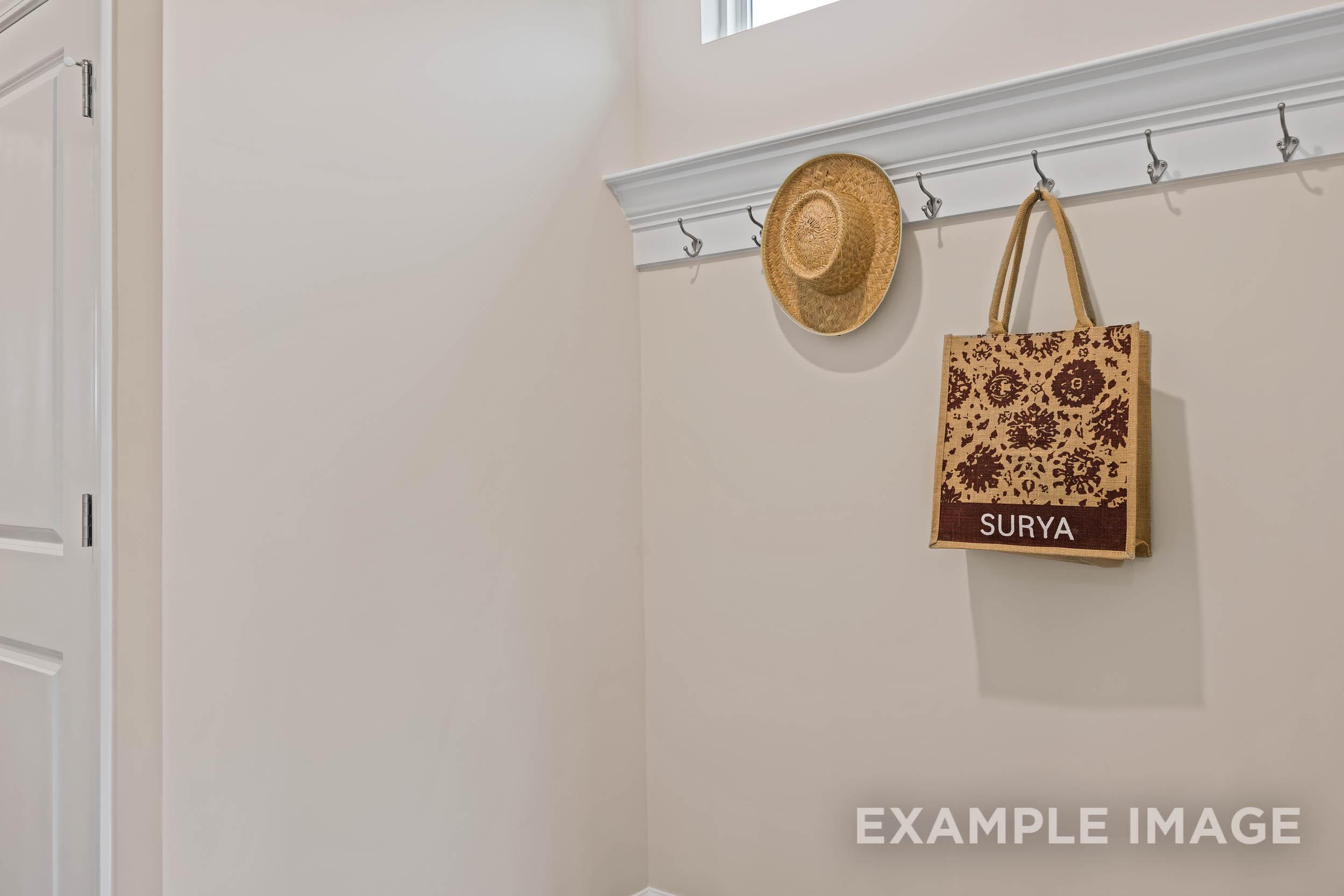 Cozy entryway in The Preston A home design with wall hooks holding straw hat and Surya tote bag on beige wall