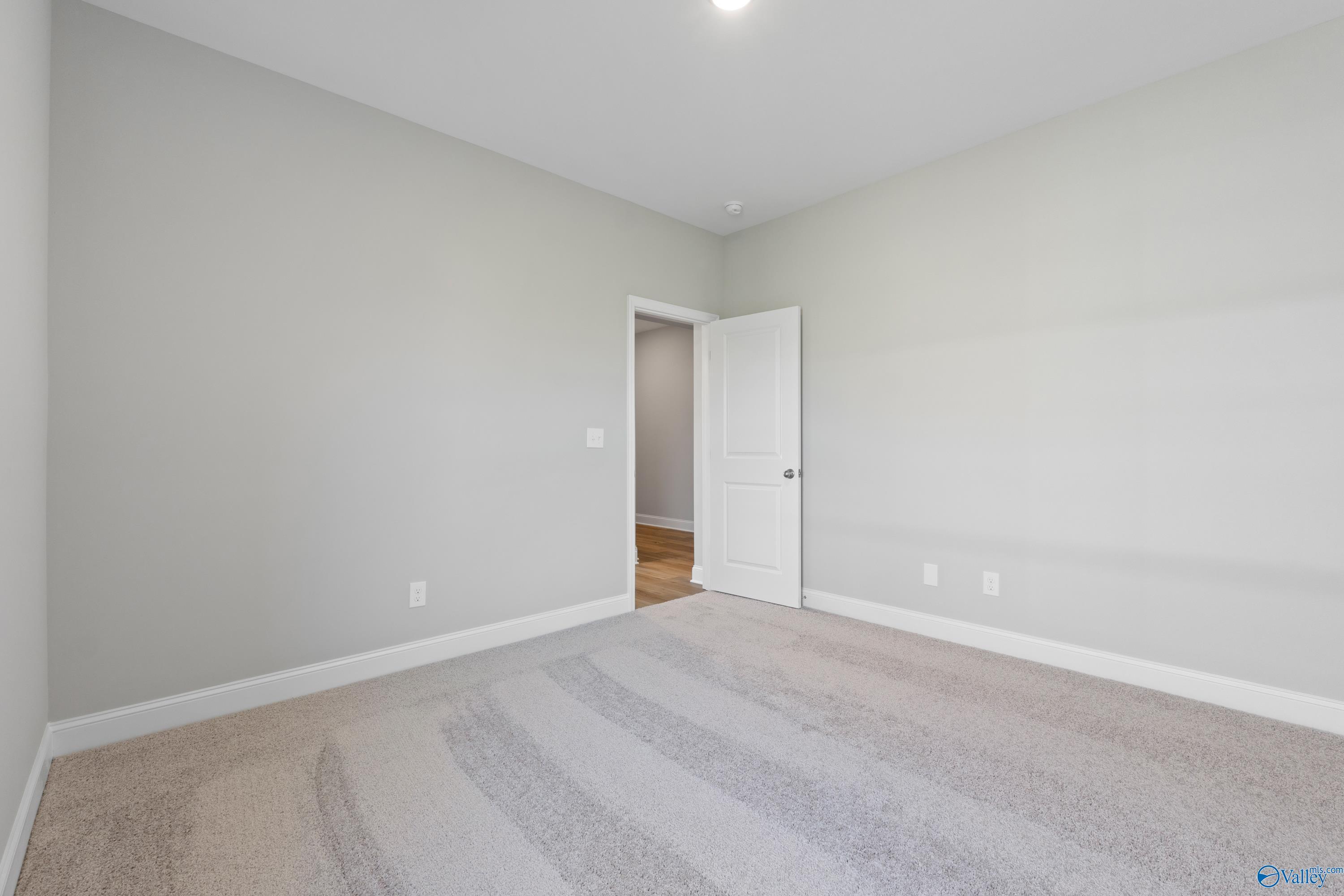 Empty bedroom with light gray walls, beige carpet, and open door to hardwood hallway in Davidson Homes Everett B, Toney, Alabama