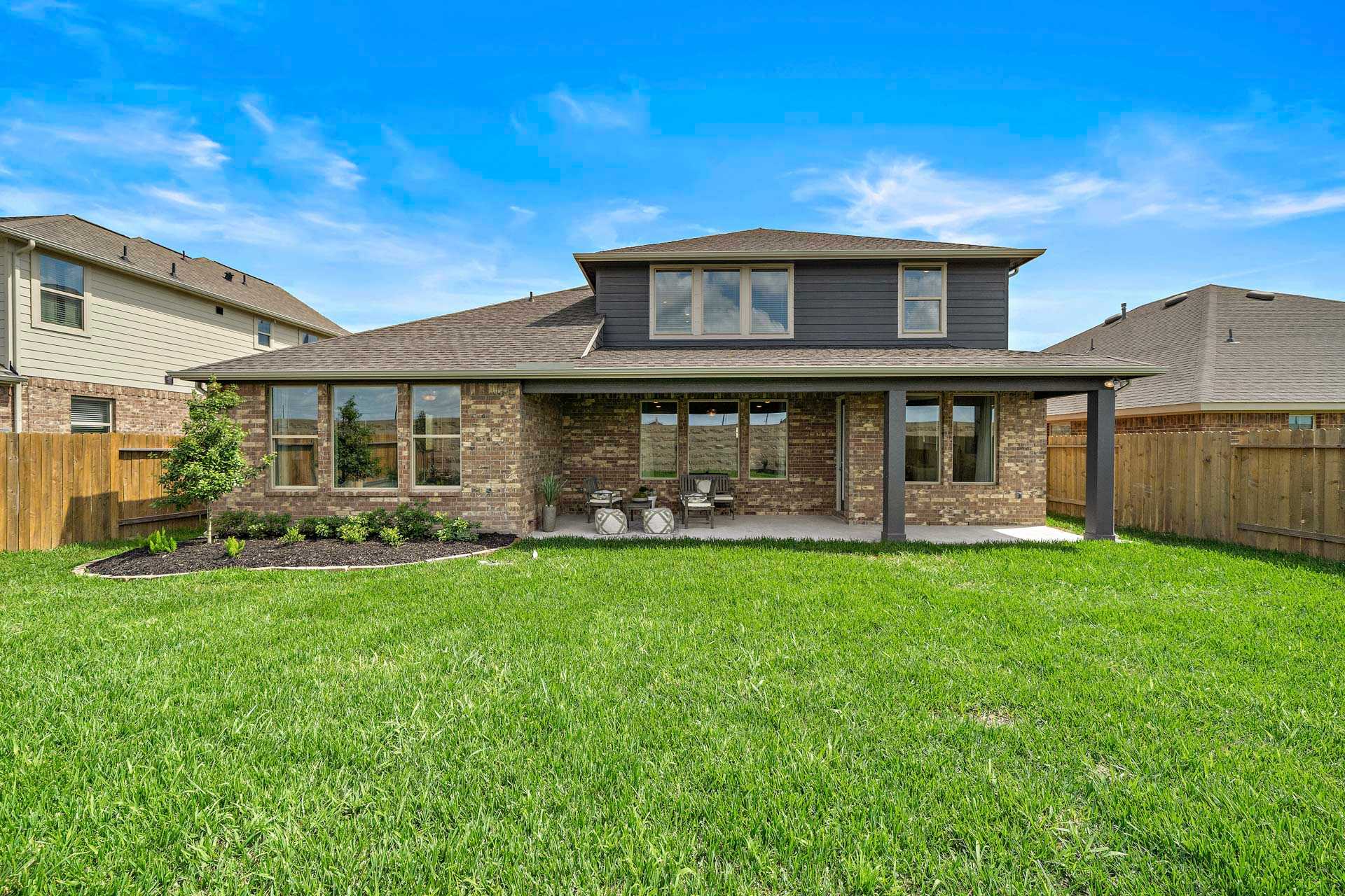 Two-story home backyard patio with large windows, brick exterior, lush green lawn at Sierra Vista in Rosharon Texas