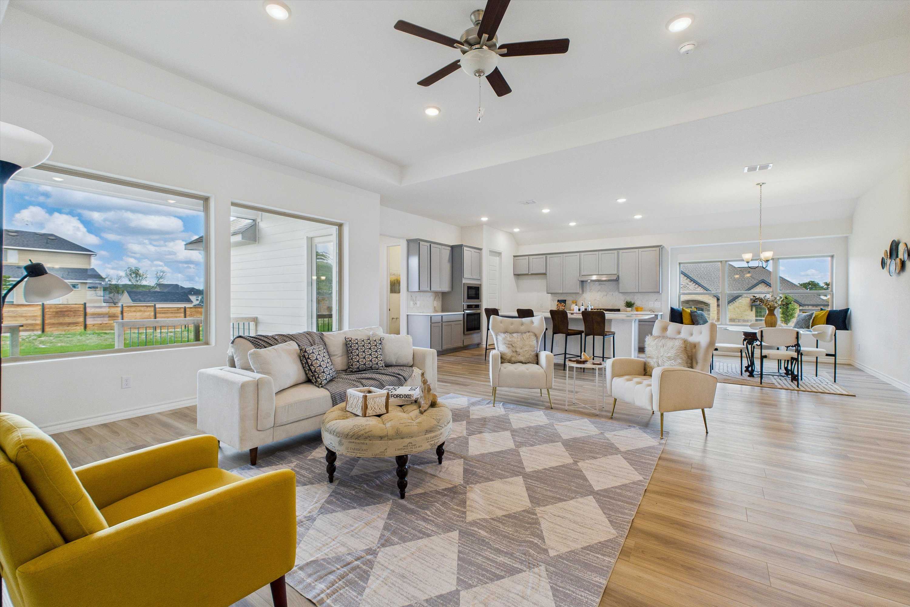 Modern open-concept living room with white sofas, yellow armchair, patterned rug, and kitchen island in Davidson Homes Summerlin C, Castroville, Texas