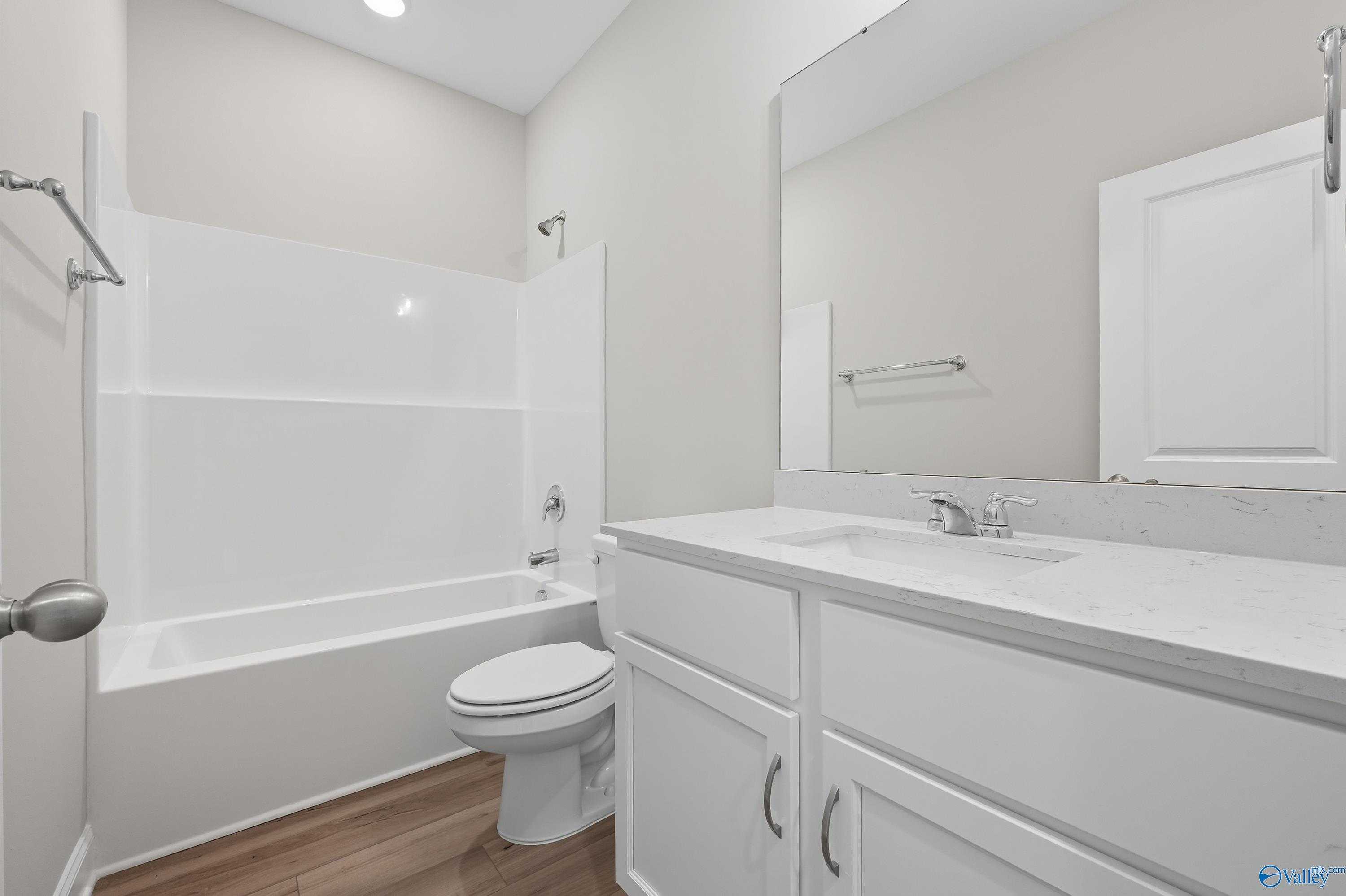 Modern bathroom with double vanity, quartz counters, tub-shower combo, and wood floors in Davidson Homes The Franklin, Meridianville, Alabama