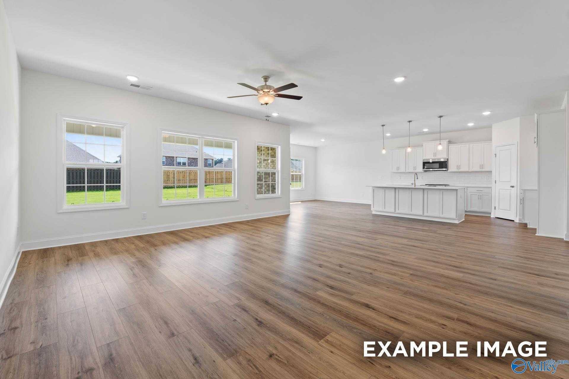 Spacious open living-kitchen with white island, luxury vinyl floors, ceiling fan, and backyard views in The Rockford B, Athens AL