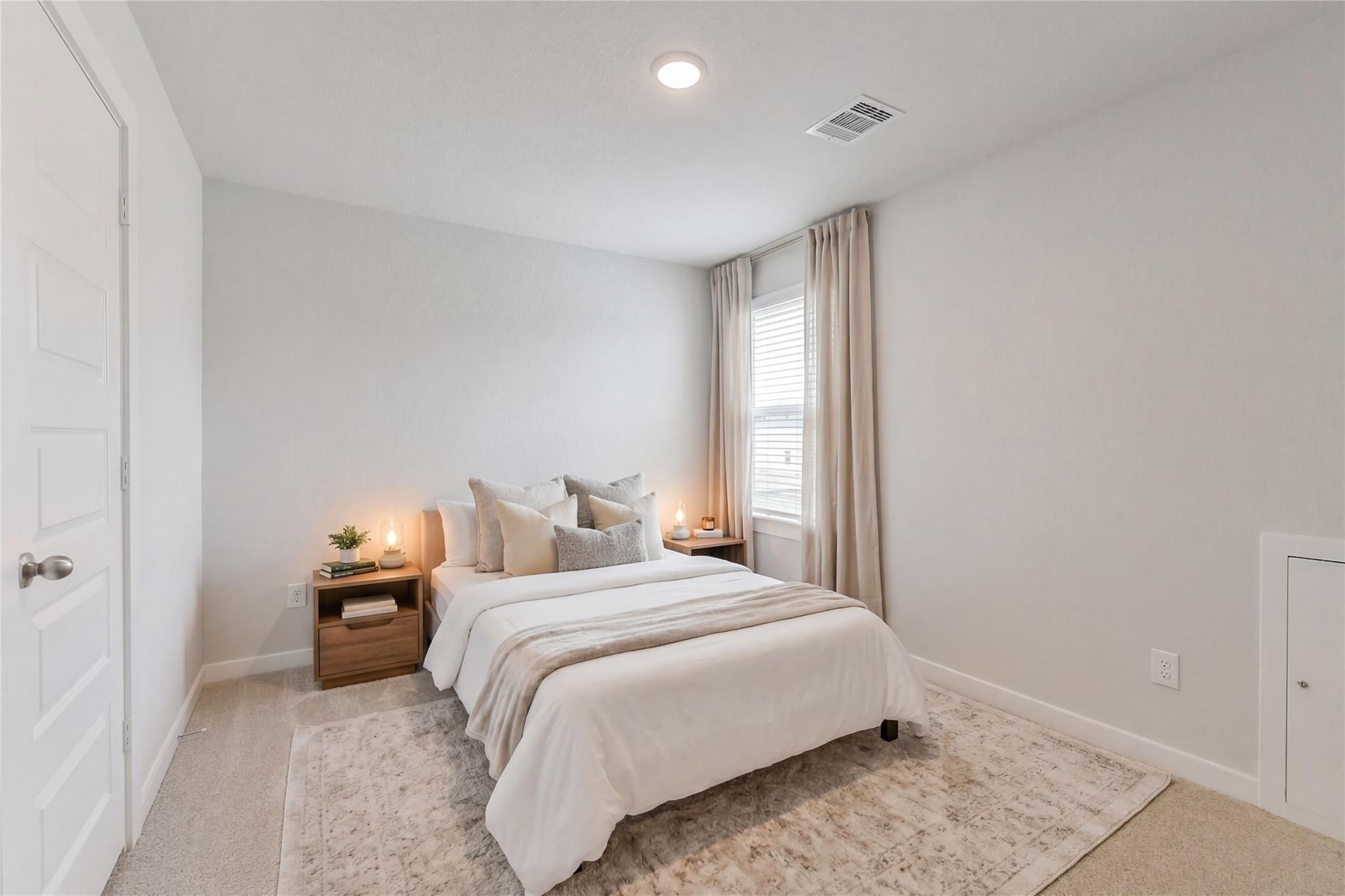 Cozy secondary bedroom with queen bed, neutral bedding, wood nightstands, and window drapes in Davidson Homes The Brazos E, Cleveland, TX