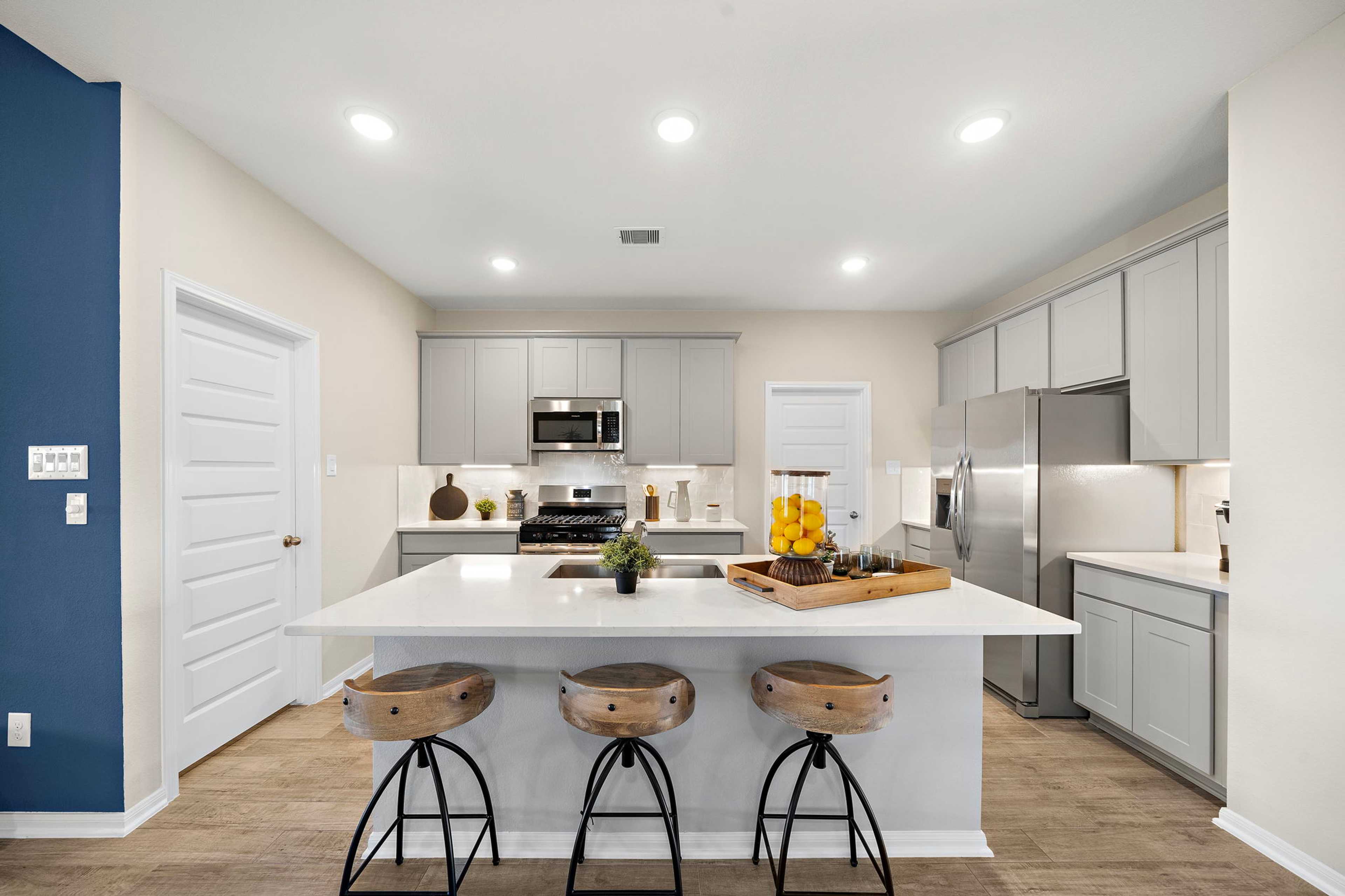 Spacious modern kitchen in Emberly Beasley TX with white quartz island, wooden bar stools, gray cabinets, stainless appliances