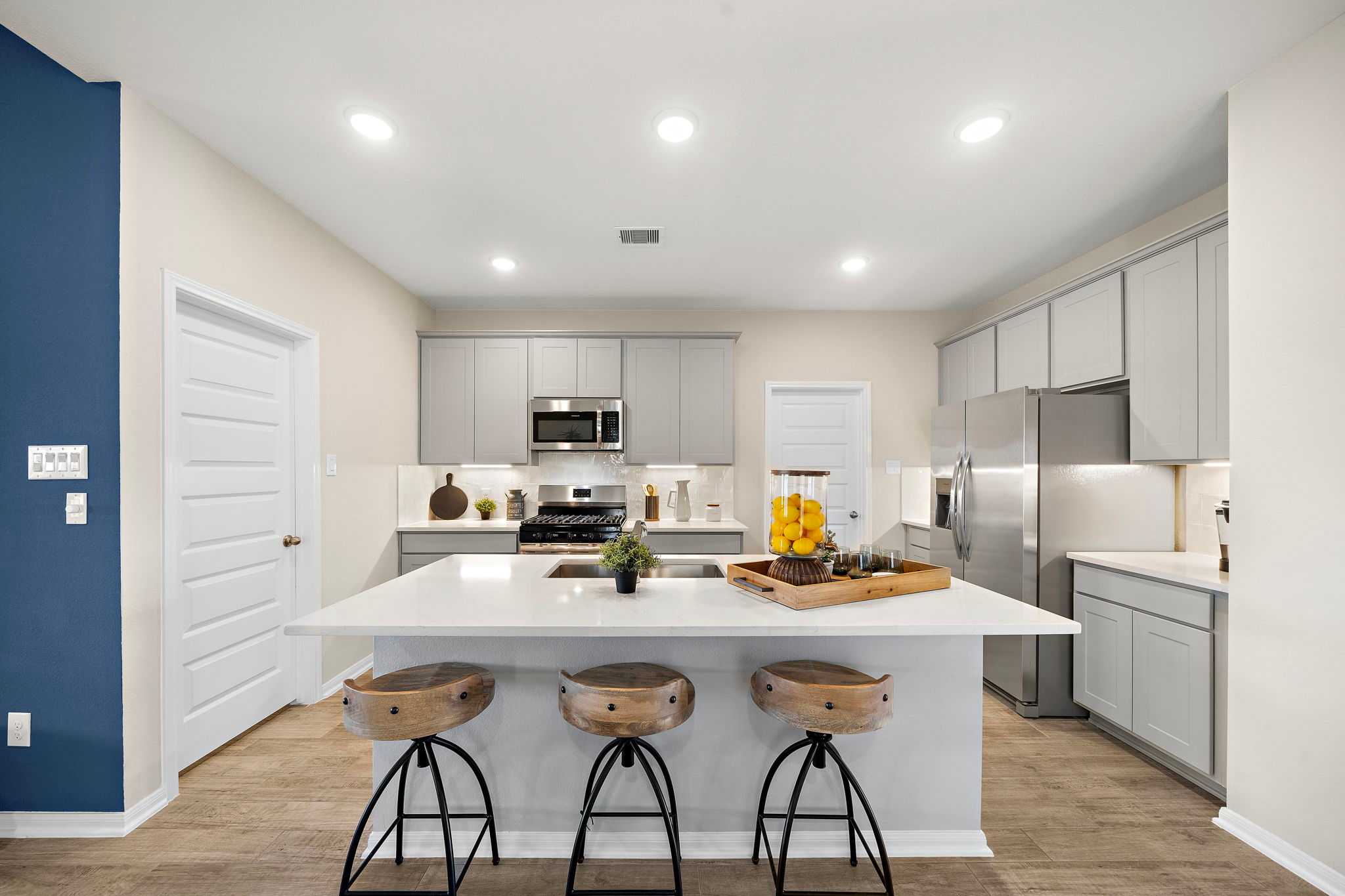 Spacious modern kitchen in Emberly Beasley TX with white quartz island, wooden bar stools, gray cabinets, stainless appliances
