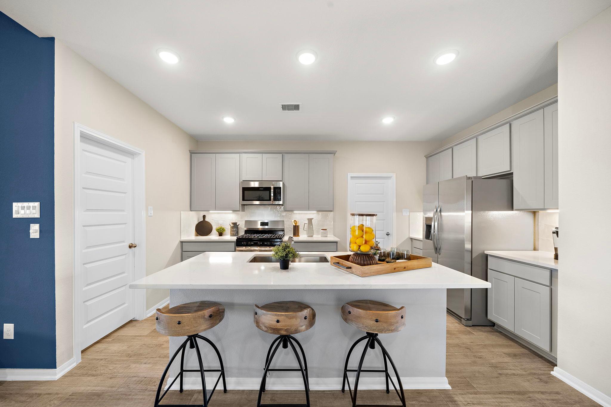 Spacious modern kitchen in Emberly Beasley TX with white quartz island, wooden bar stools, gray cabinets, stainless appliances
