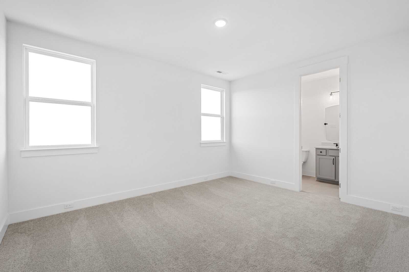 Bright bedroom with en-suite bath, white walls, large windows, and carpeted floor in Davidson Homes The Alston A, Murfreesboro, TN