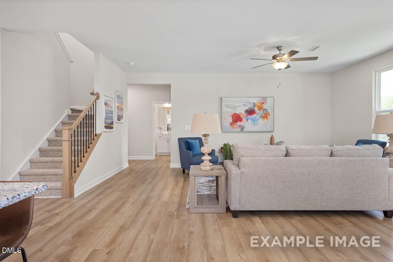 Spacious living room with oak staircase, beige sectional sofa, blue armchair, abstract art, and hardwood floors in The Willow D, Lillington, NC