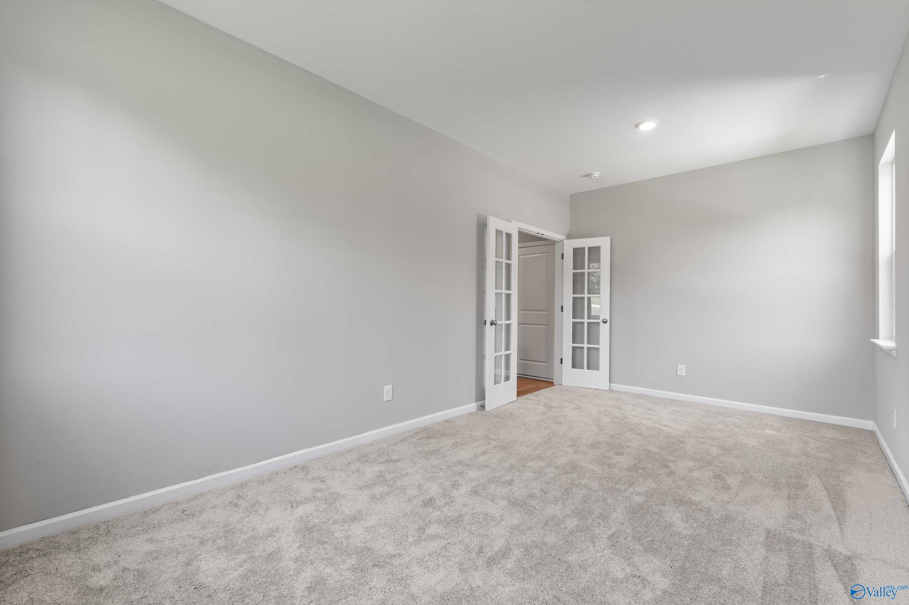 Spacious empty room with light gray walls, beige carpet, French doors, and large window in Davidson Homes The Charm, Huntsville, Alabama