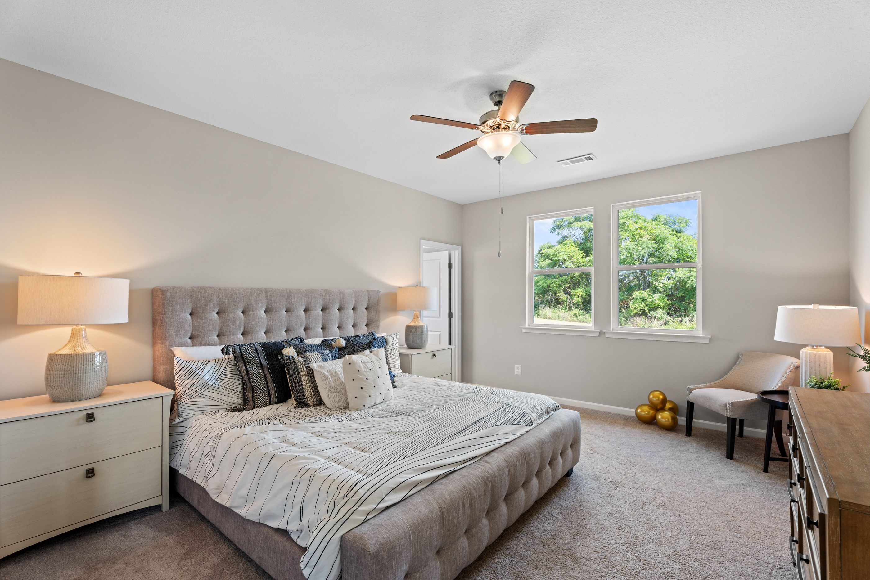 Spacious master bedroom in Ivy Glen Perry Georgia with tufted gray bed, ceiling fan, and large windows overlooking trees