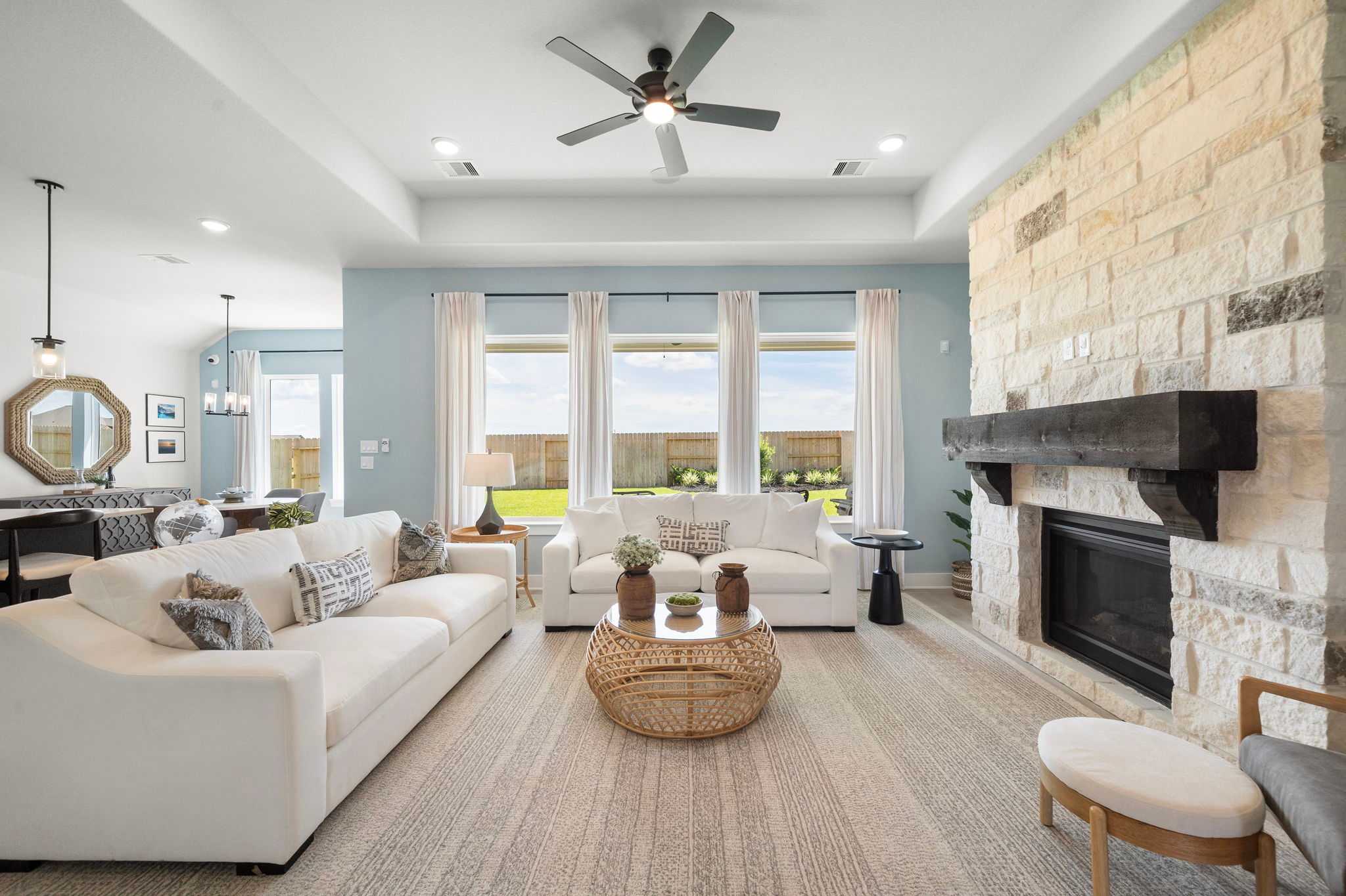 Open-concept living room at Lago Mar in Texas City Texas with white sofas stone fireplace large windows and rattan coffee table