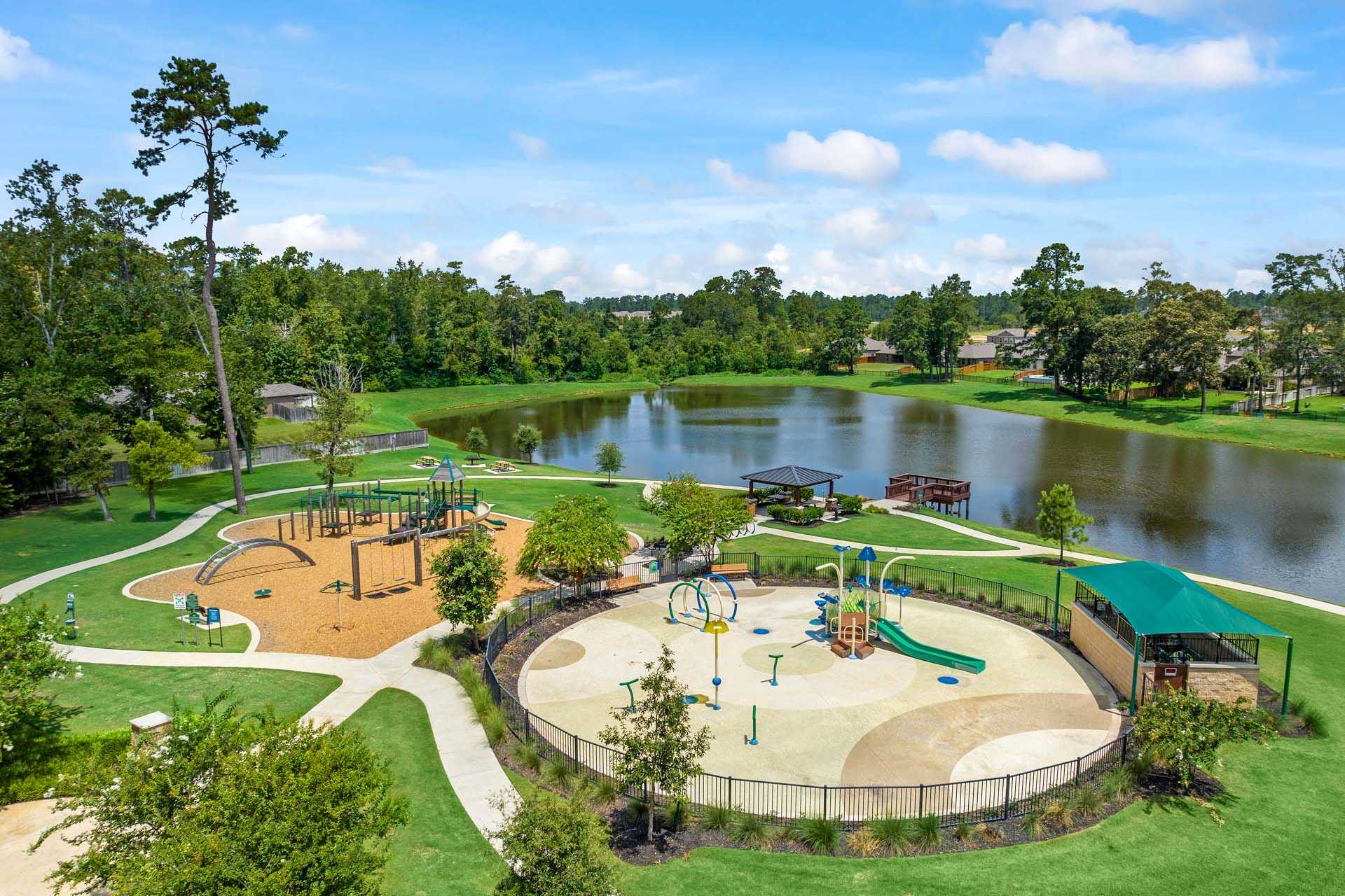 Vibrant playground and splash pad at Lakes at Black Oak in Magnolia Texas featuring slides swings lake pond and shaded pavilion