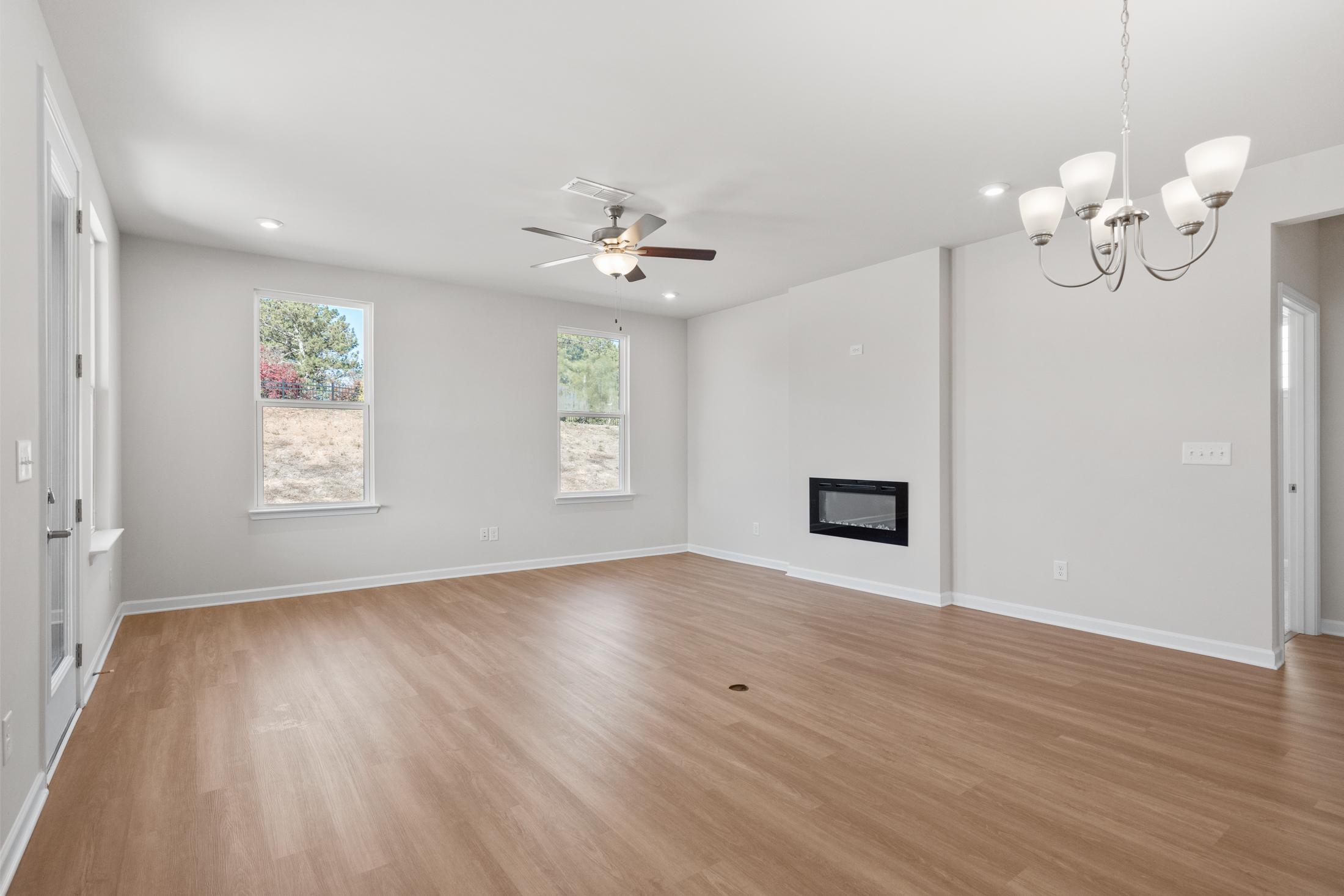 Spacious open-concept living room in The Dawson B with hardwood floors, ceiling fan, chandelier, and linear fireplace