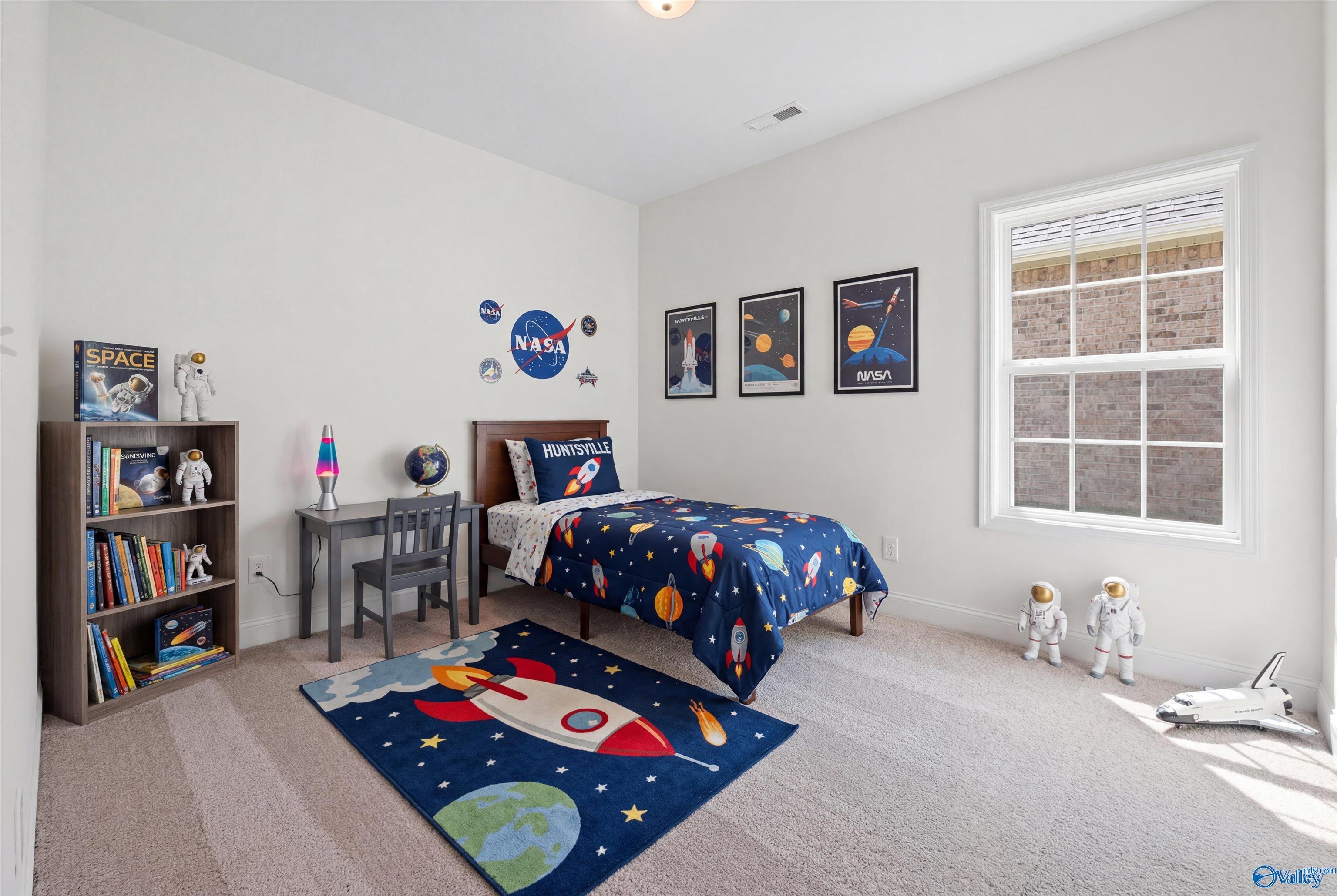 Space-themed kids' bedroom with galaxy bed, rocket rug, NASA posters, and bookshelf in Davidson Homes The Rockford B, Toney, Alabama