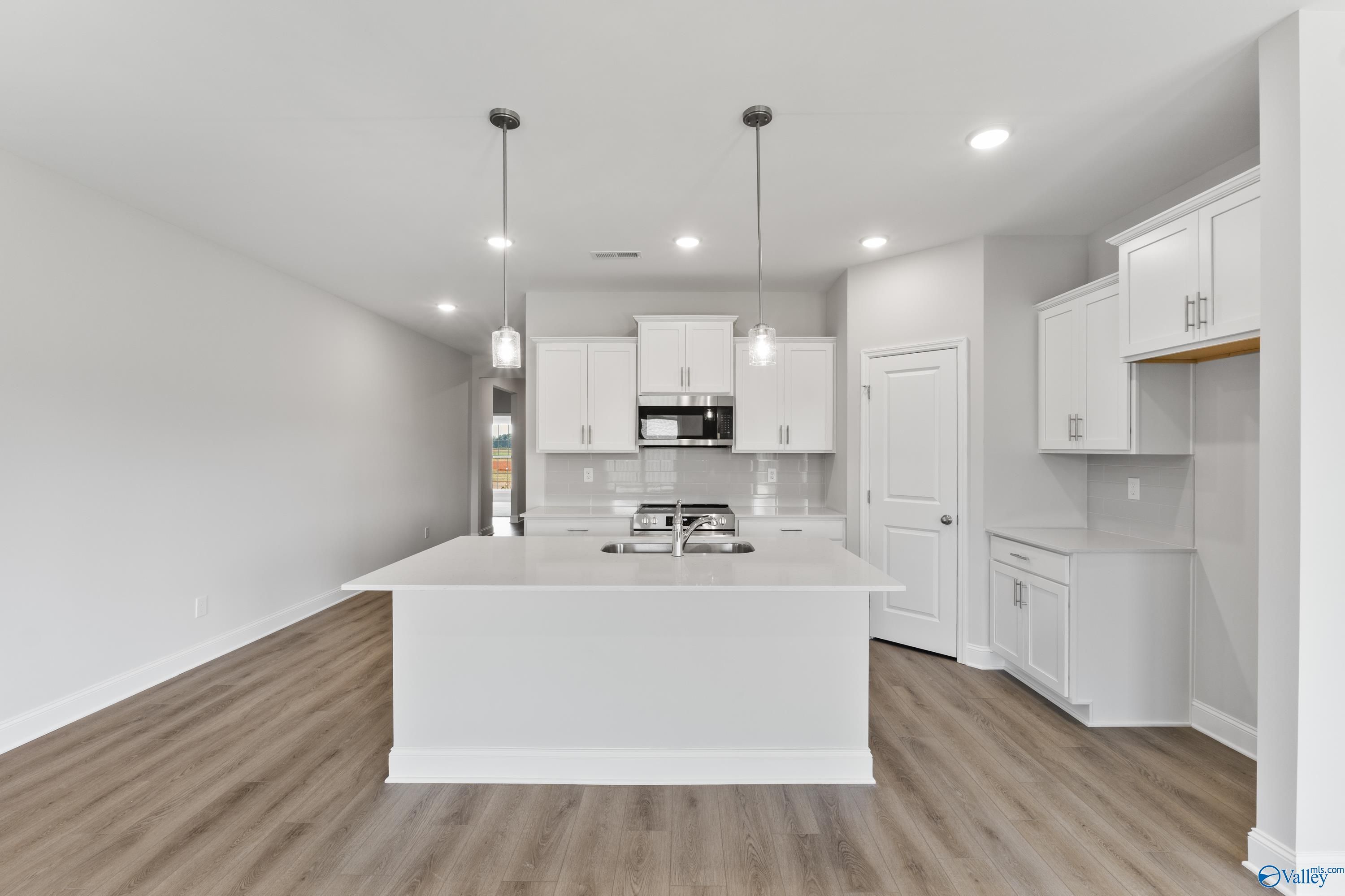 Modern white kitchen with large island, stainless steel appliances, and pendant lights in Davidson Homes The Daphne, Hazel Green, AL
