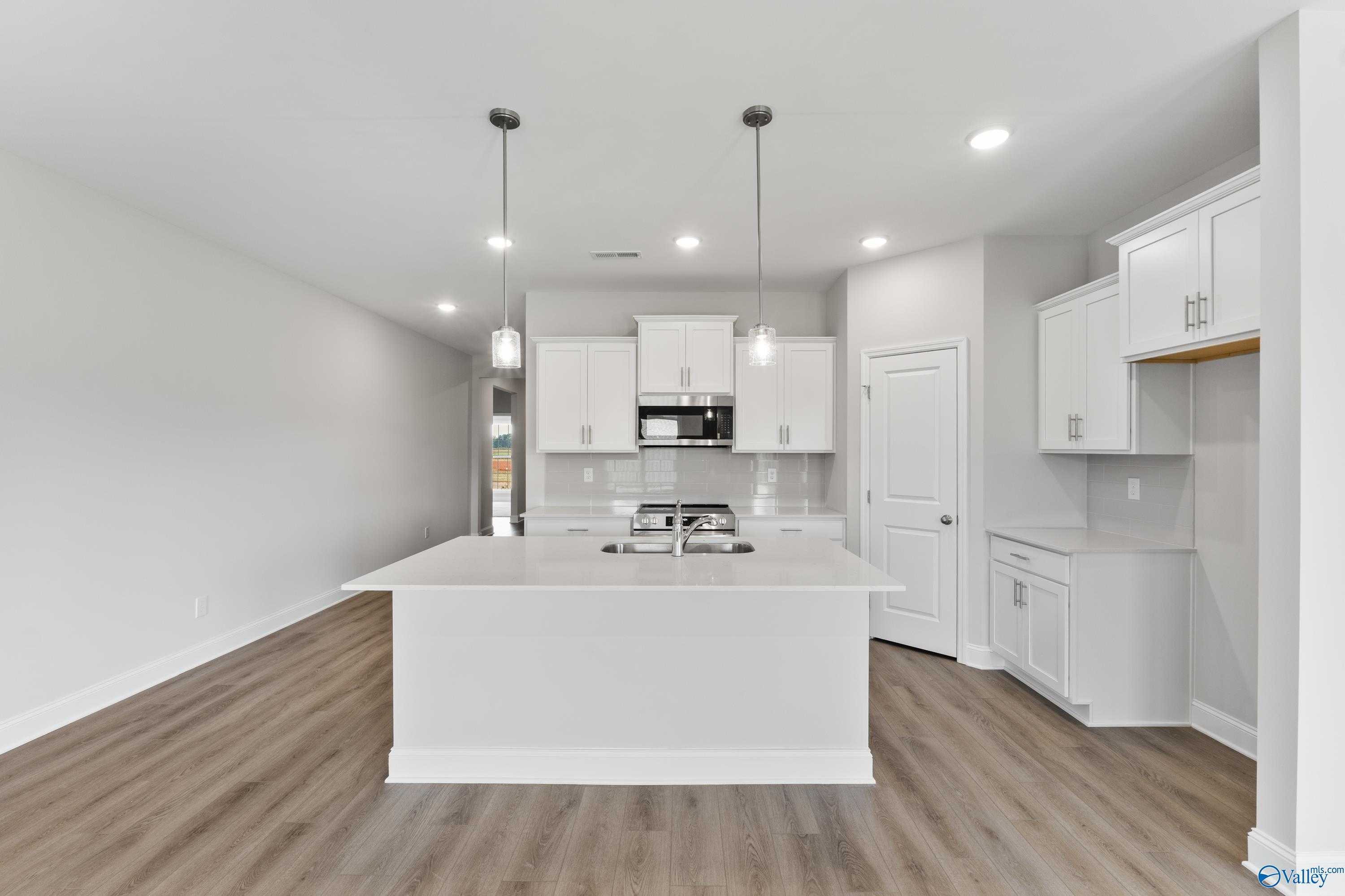 Modern white kitchen with large island, stainless steel appliances, and pendant lights in Davidson Homes The Daphne, Hazel Green, AL