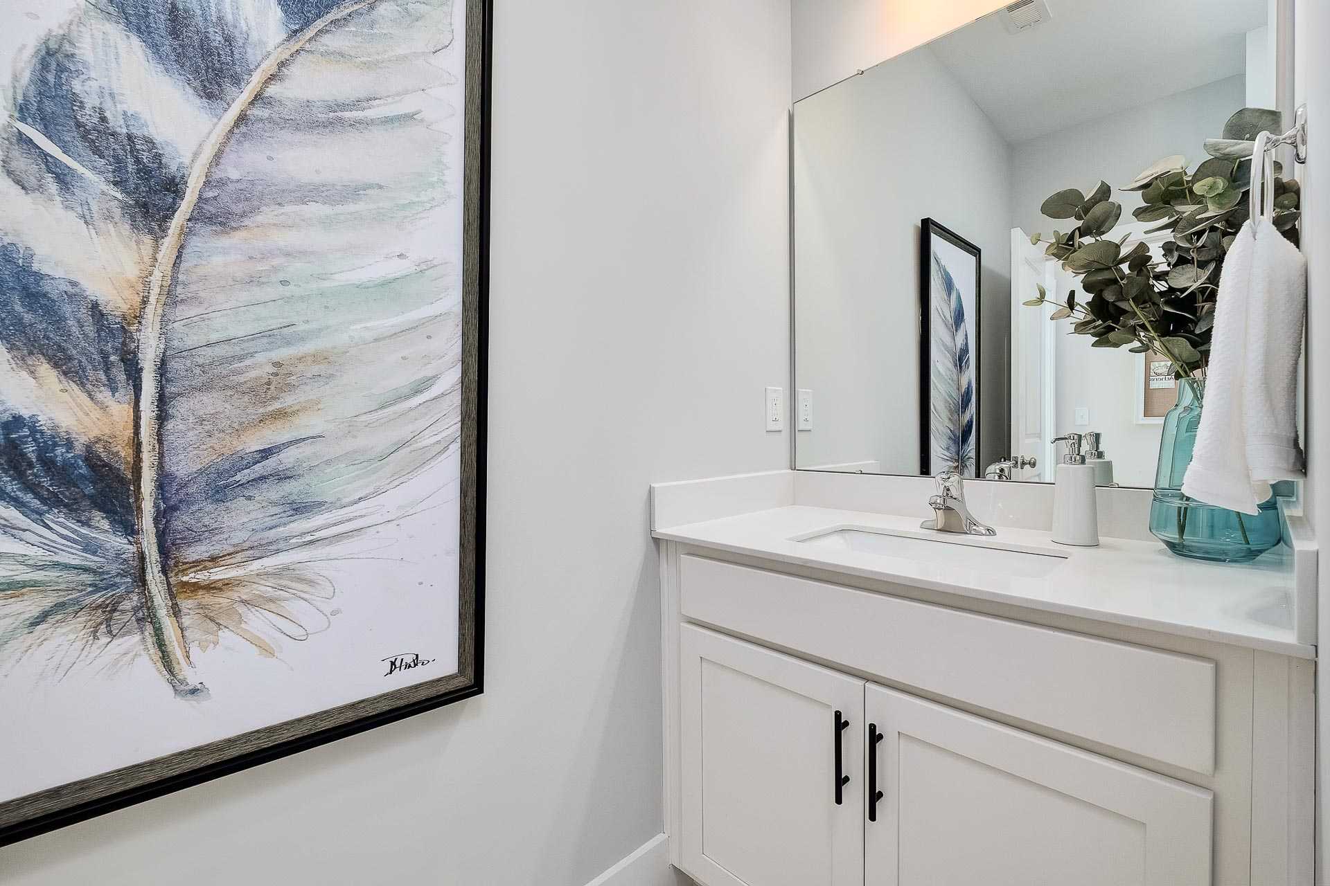 Modern bathroom with white vanity, frameless mirror, eucalyptus accents, and abstract feather artwork in Newby Chapel, Athens Alabama