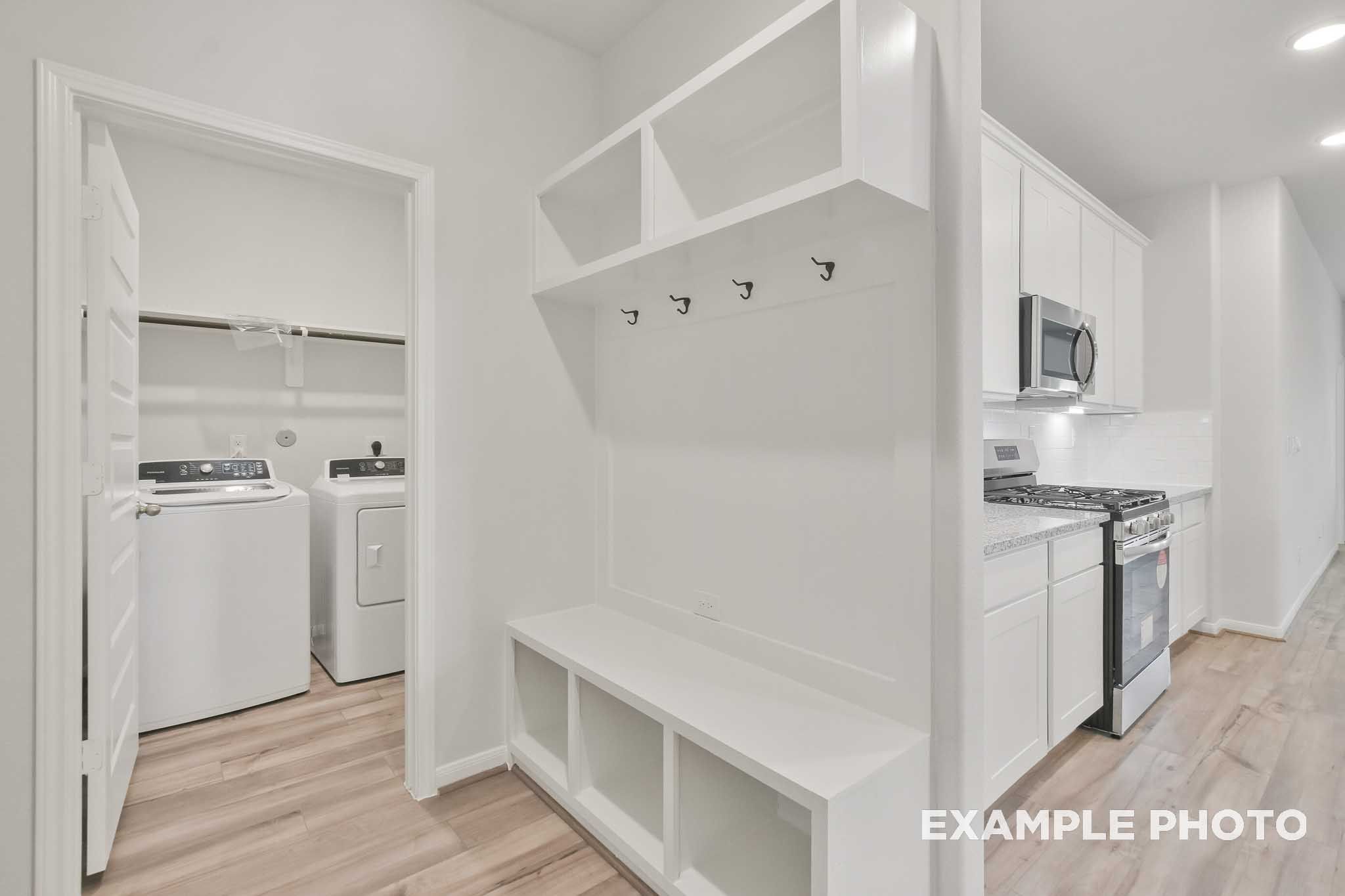 Mudroom with built-in bench and coat hooks beside laundry room and white kitchen in The Brazos by Davidson Homes, Beasley TX