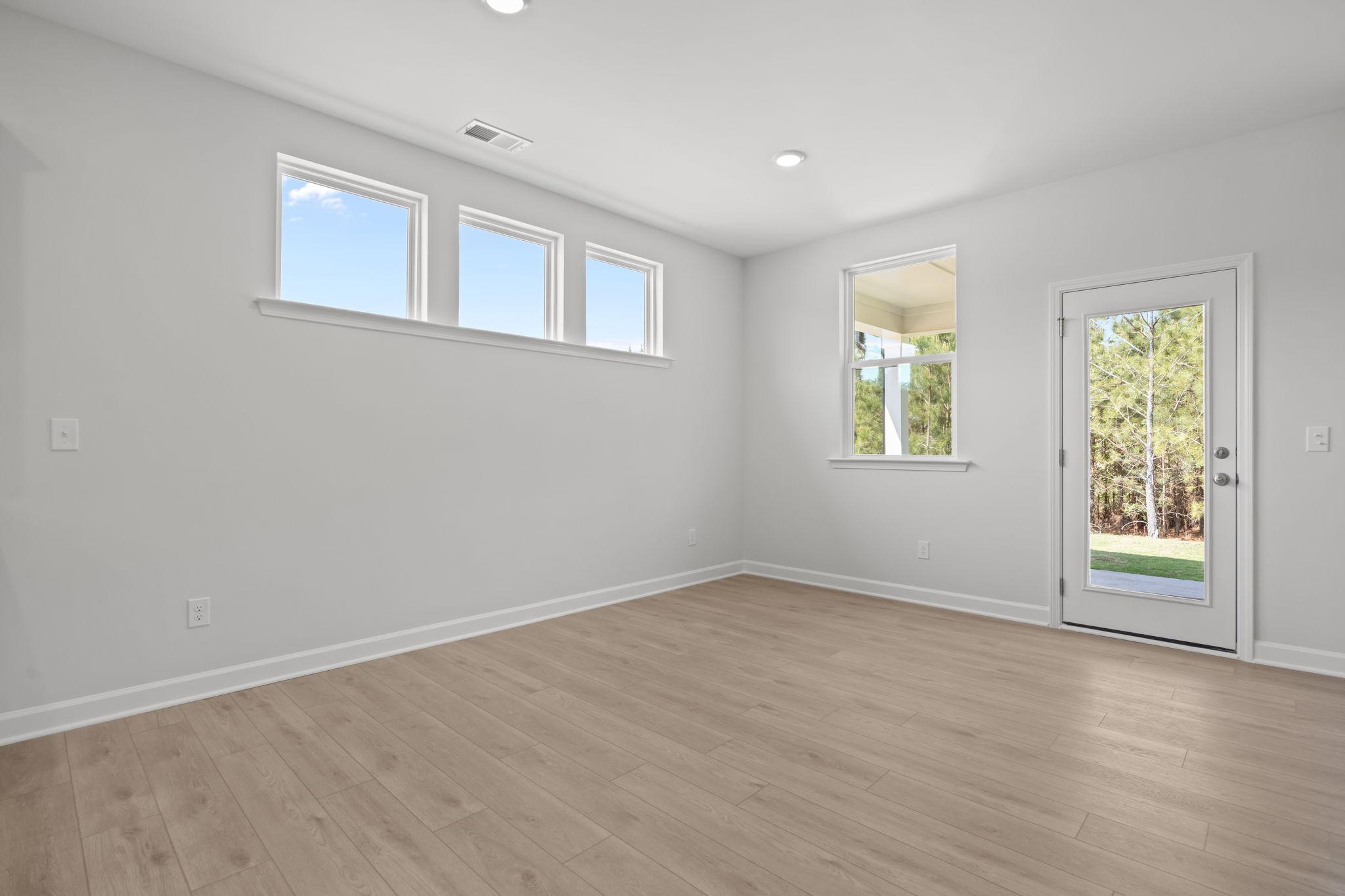 Bright, open living space in The Ashport B with light wood flooring, natural light, and glass door access to the backyard.