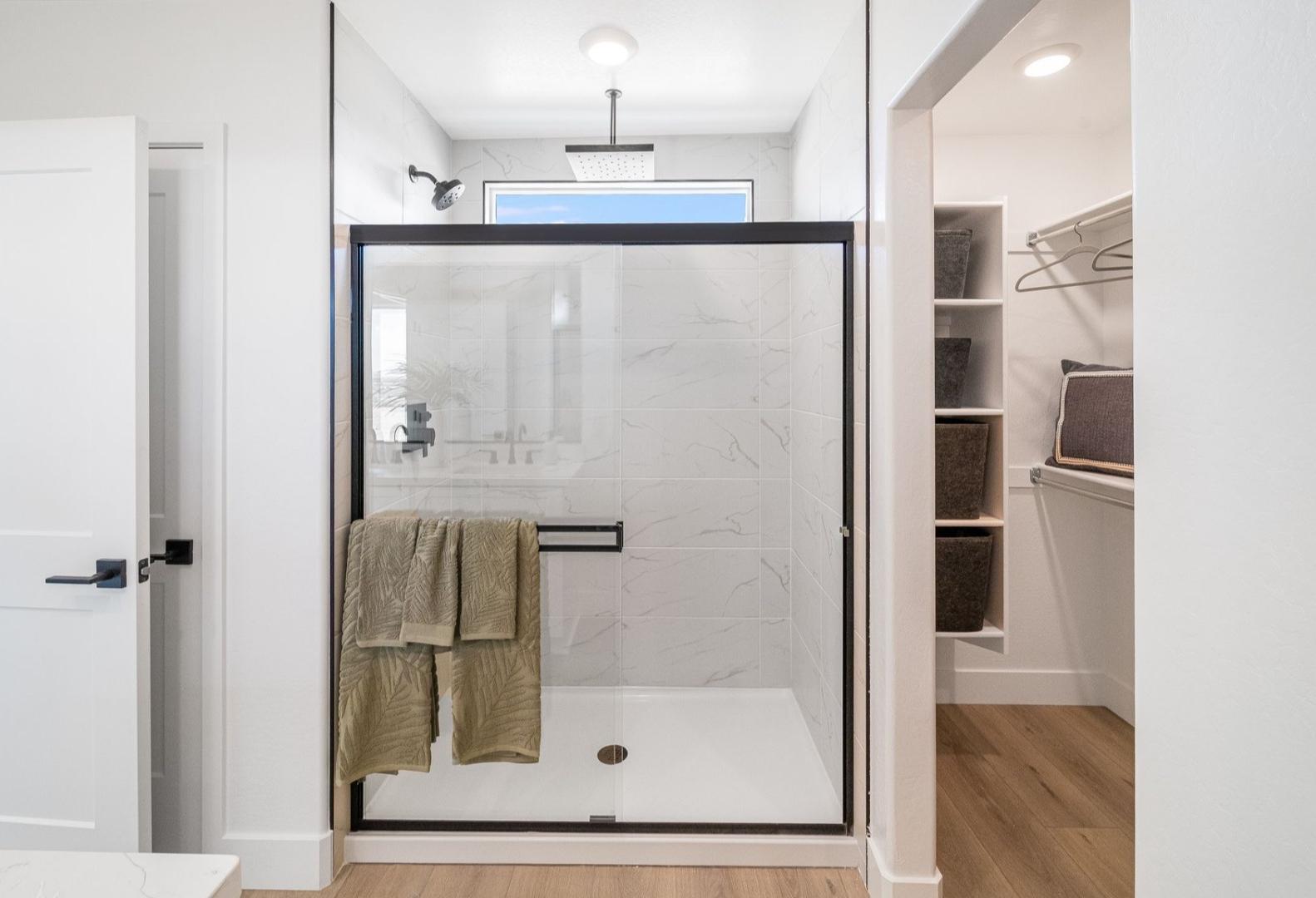 Modern master bathroom in The Wilmington A featuring frameless glass shower with subway tiles, bench, and adjacent walk-in closet