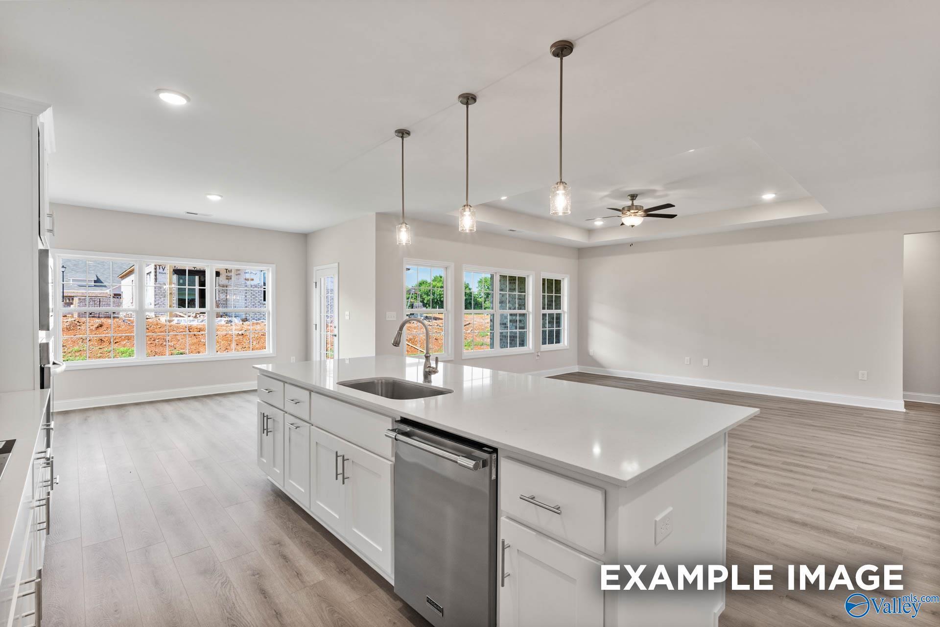 Modern open-concept kitchen with white quartz island, sink, stainless dishwasher, pendant lights, and backyard views in Davidson Homes Finleigh, Huntsville AL