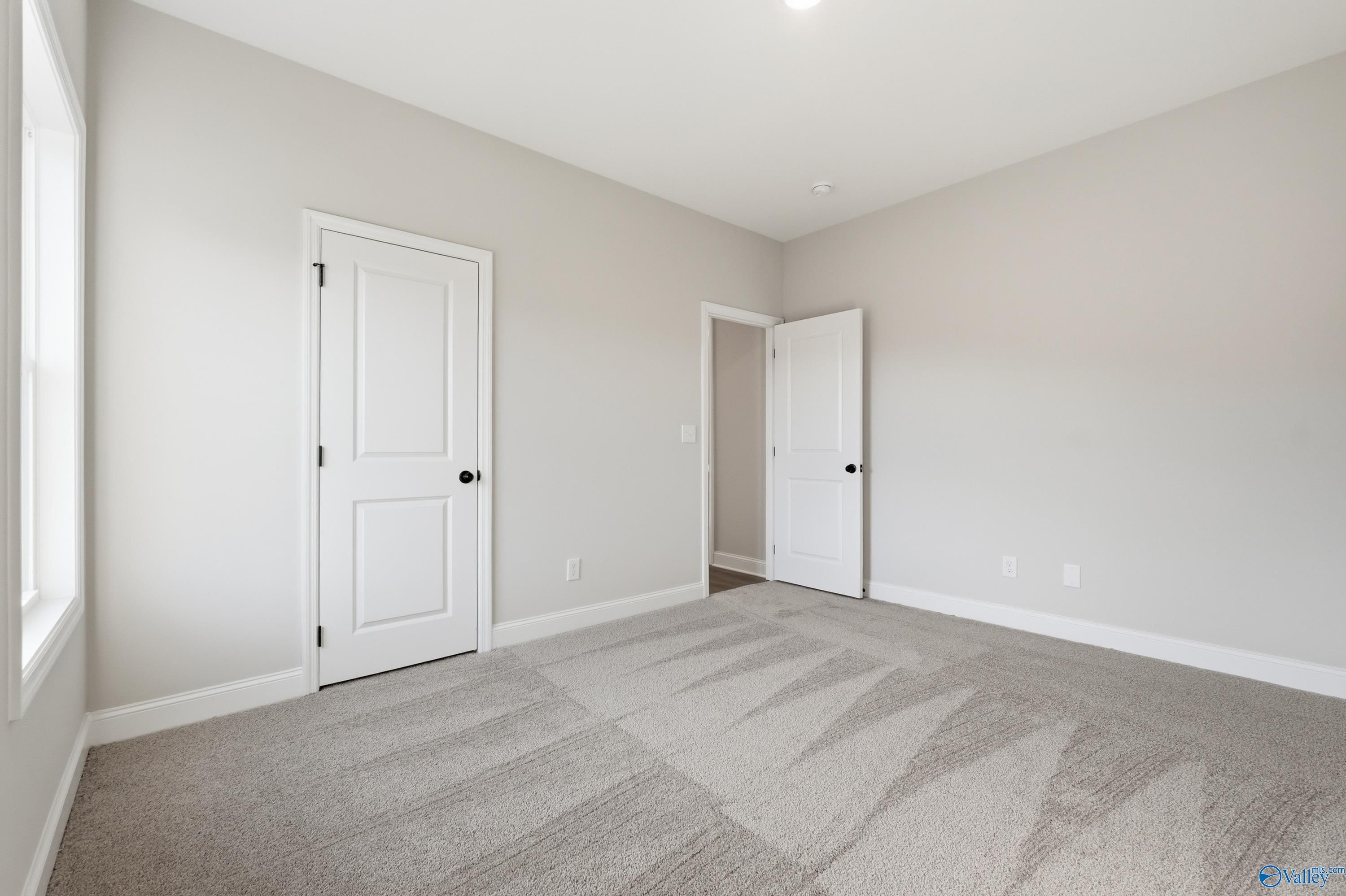 Spacious secondary bedroom with neutral beige walls, white doors, and gray carpet in Davidson Homes The Daphne D, Arab, Alabama