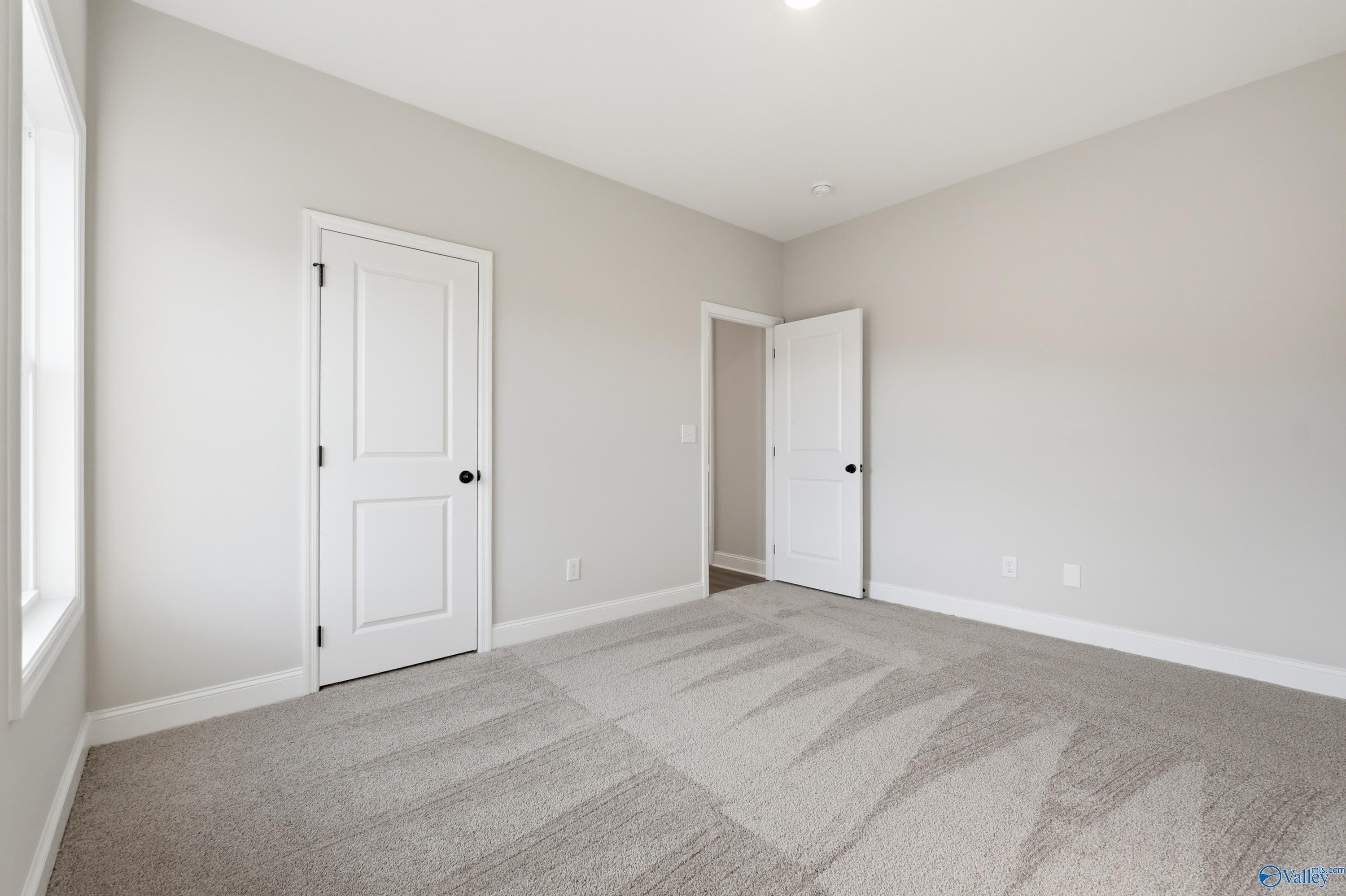 Spacious empty bedroom with gray carpet, white doors, and neutral walls in The Daphne D 4-bedroom home, Arab, Alabama