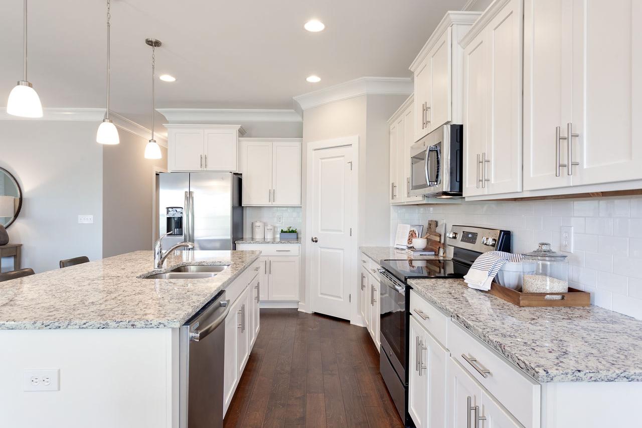 Spacious white kitchen in The Rockford with granite countertops, stainless steel appliances, and hardwood floors