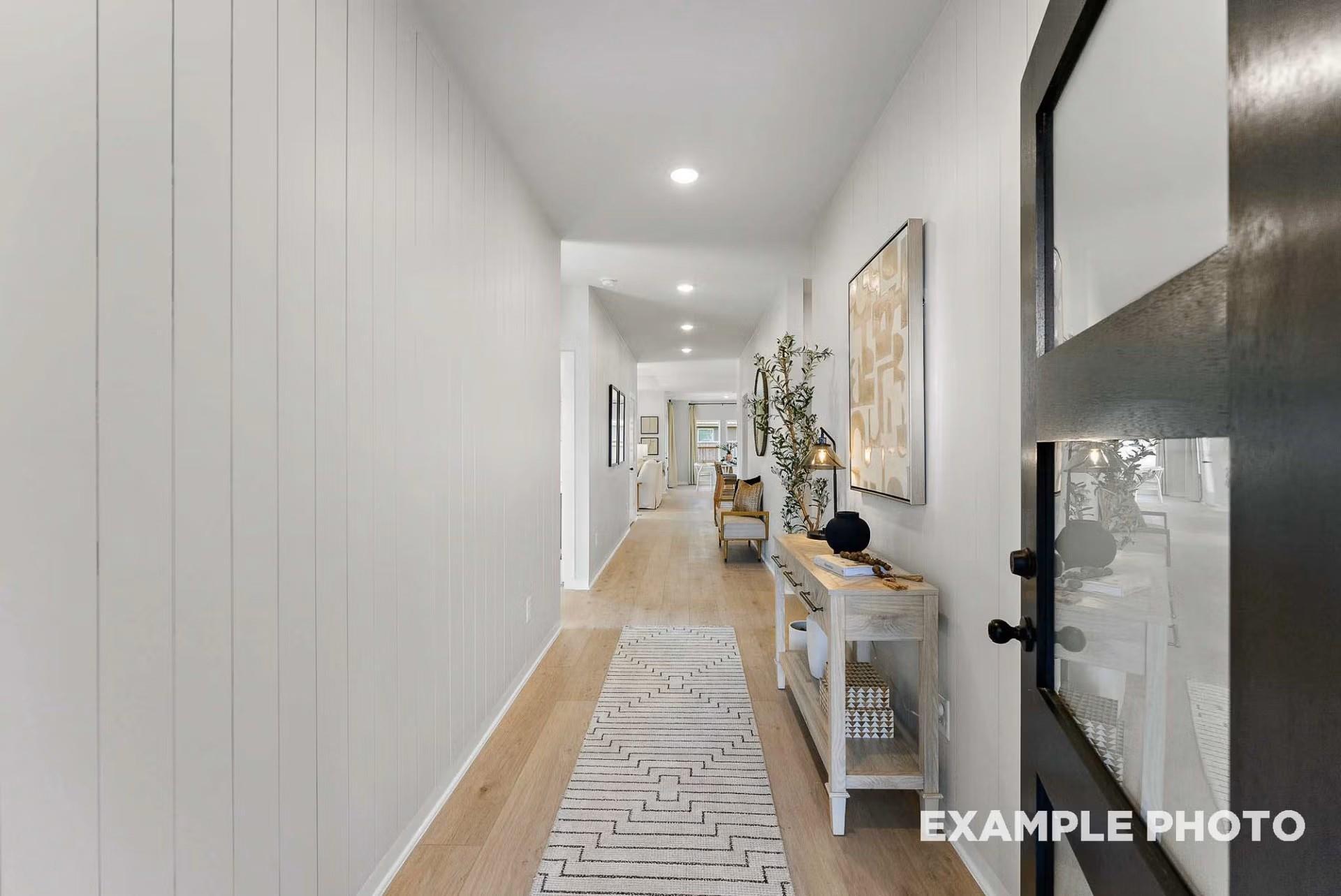 Elegant hallway with white shiplap walls, oak hardwood floors, patterned runner rug, and console table in Davidson Homes Everett C, Dayton Texas