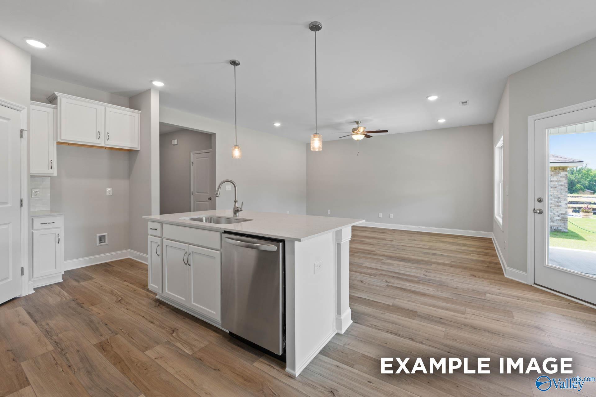 Modern open-concept kitchen with white island, stainless dishwasher, pendant lights, and backyard view in Davidson Homes Everett B, Athens AL