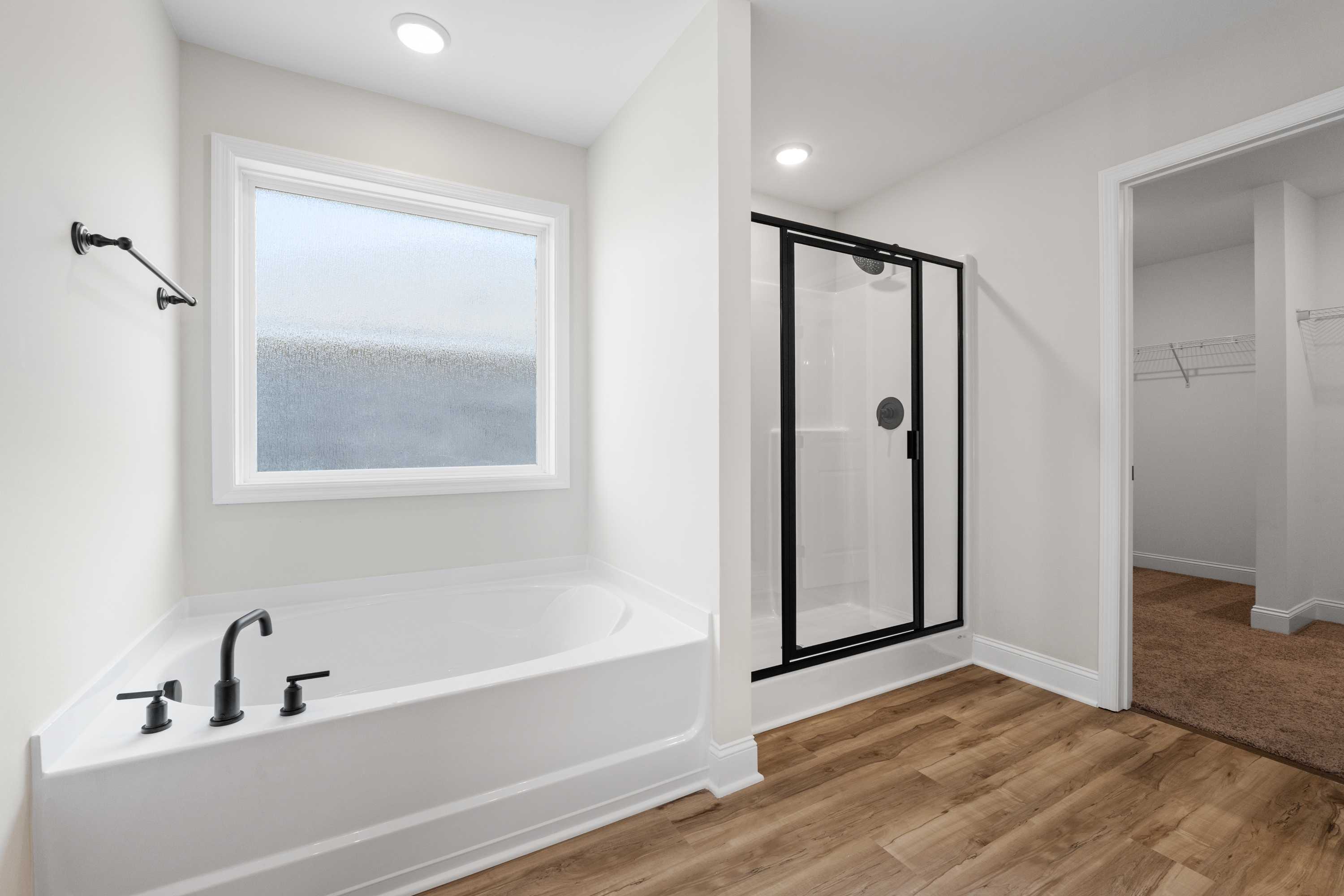 Spacious master bathroom in The Everett C with freestanding soaking tub, glass walk-in shower, and frosted window