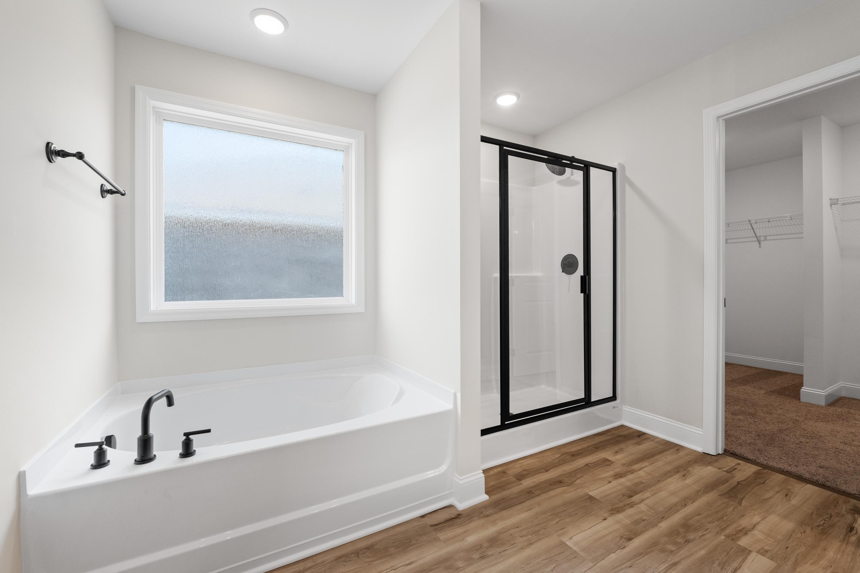 Spacious master bathroom in The Everett with freestanding soaking tub, glass walk-in shower, large frosted window, and walk-in closet