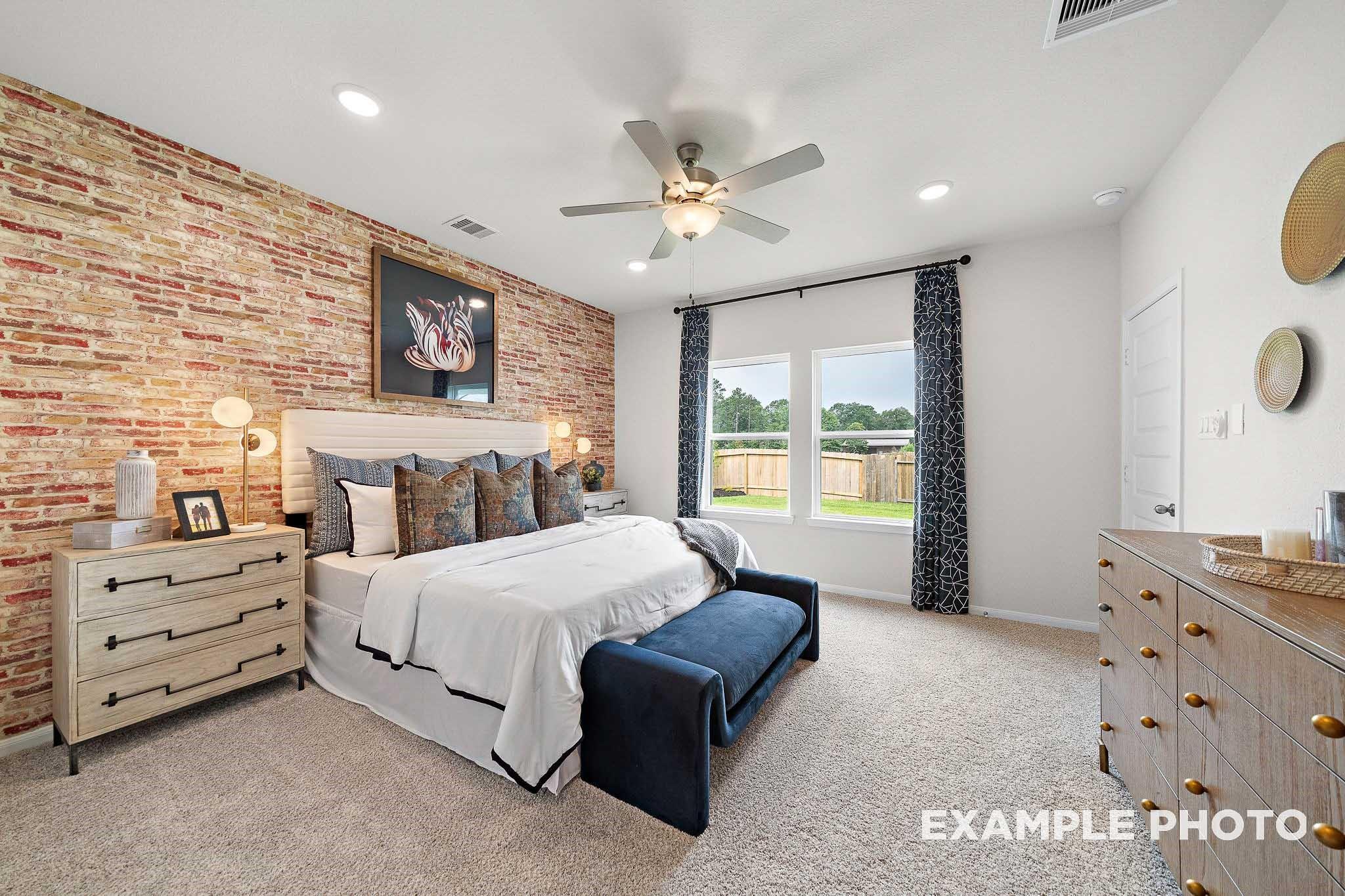 Cozy master bedroom with brick accent wall, king bed, ceiling fan, and backyard views in Davidson Homes San Marcos E, Conroe TX