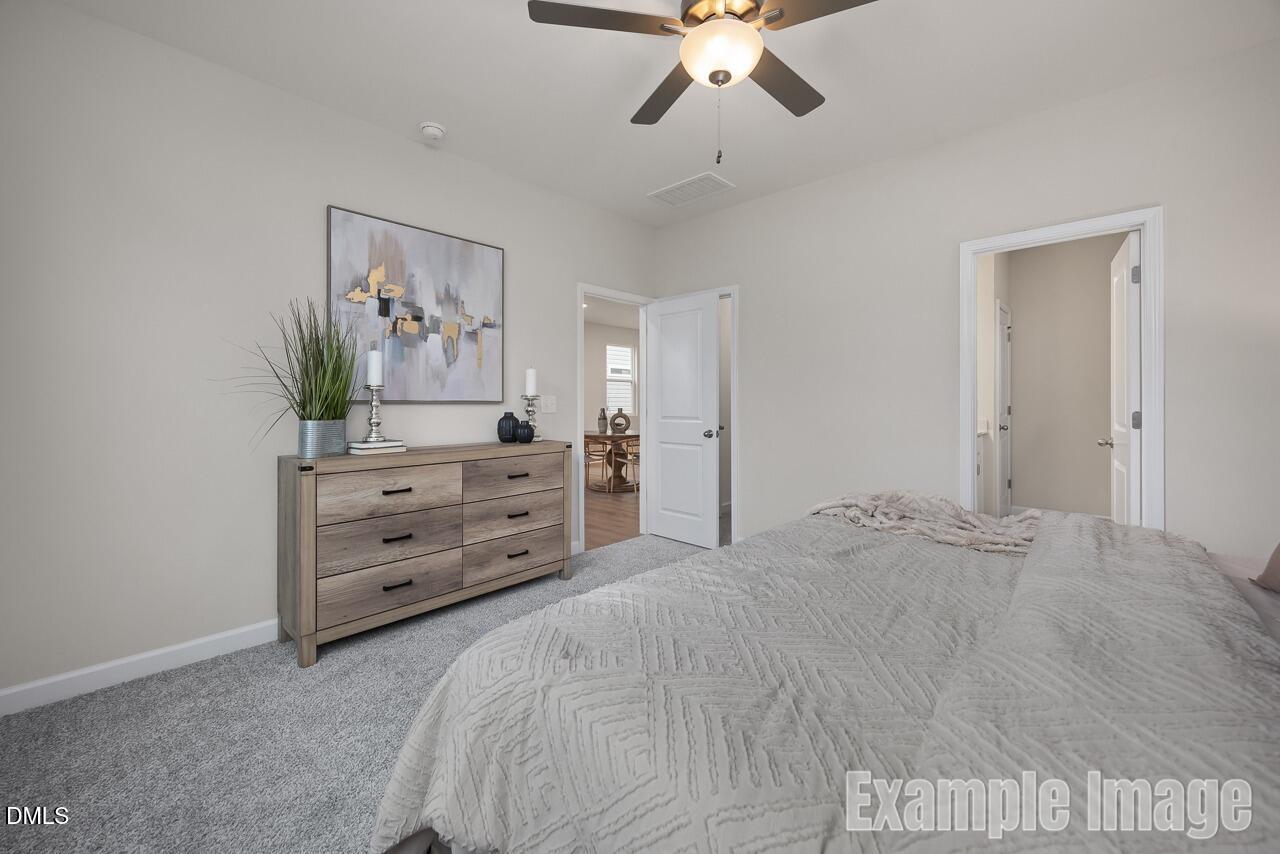 Serene master bedroom with ceiling fan, gray chevron bed, wooden dresser, abstract art, and en-suite bath in Davidson Homes The Carter C, Lillington, NC