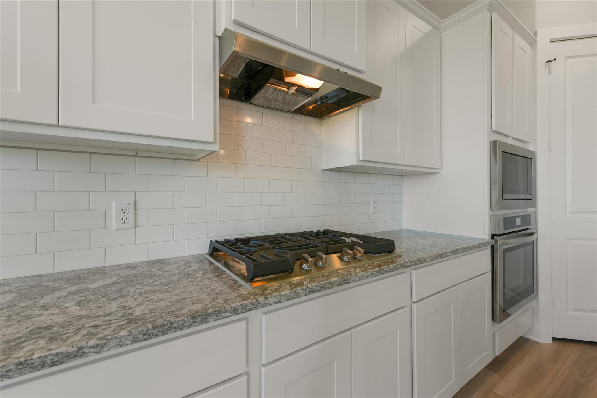 Modern kitchen with white shaker cabinets, gray granite counters, gas range, and double oven in Davidson Homes The Edward C, Lago Mar, Texas City
