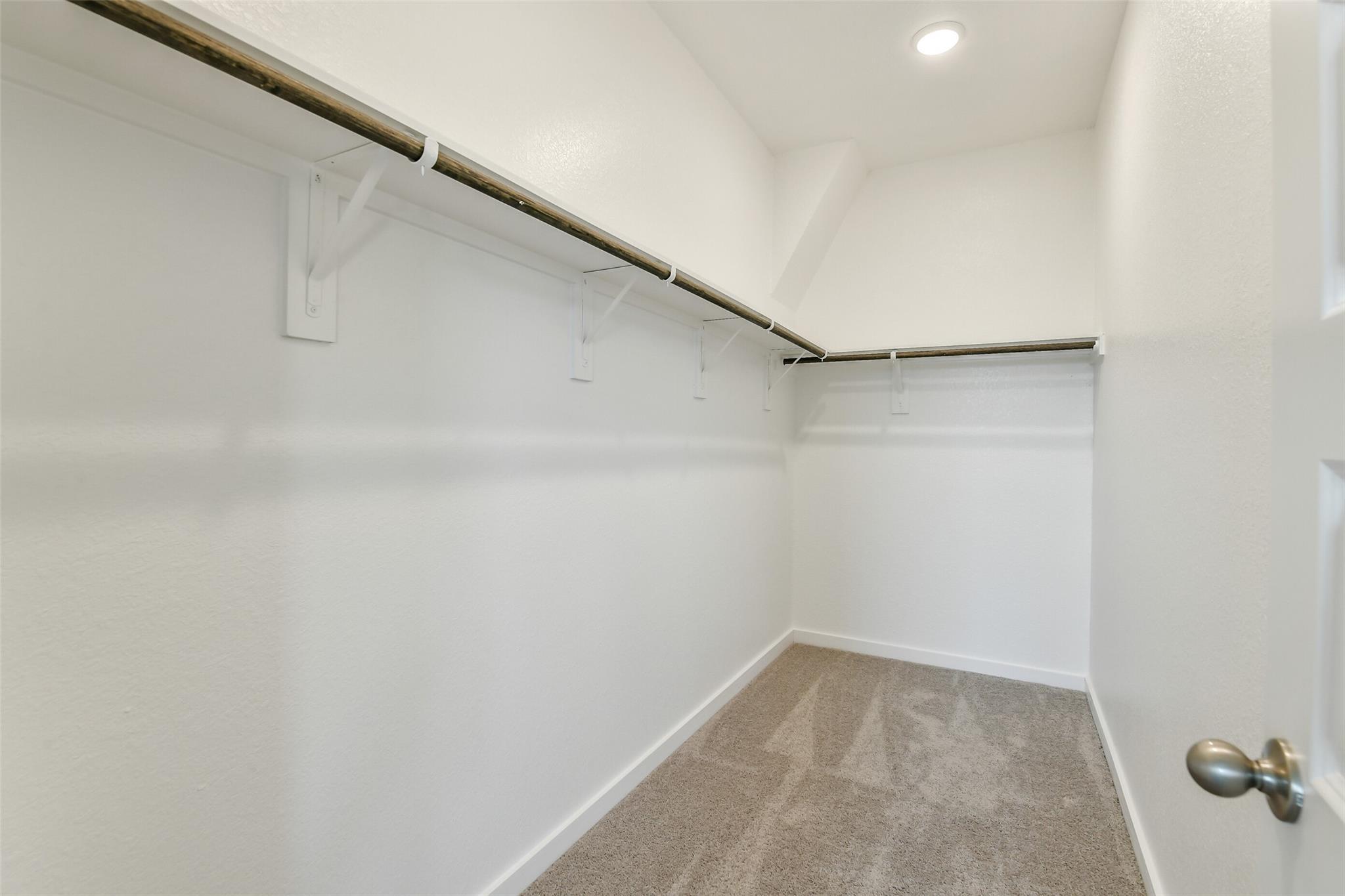 Spacious walk-in closet with white walls, built-in shelves, and hanging rods in Davidson Homes The Colorado F, Cleveland, Texas