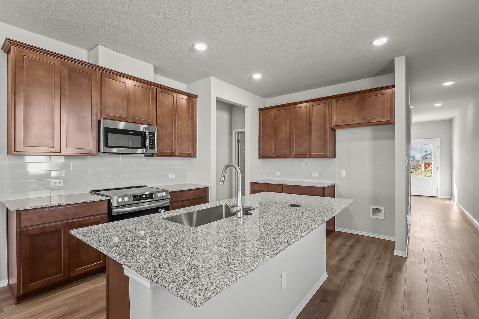 Modern kitchen with granite island, wood cabinets, and stainless appliances in The Frio G floor plan at Heartland, Texas.